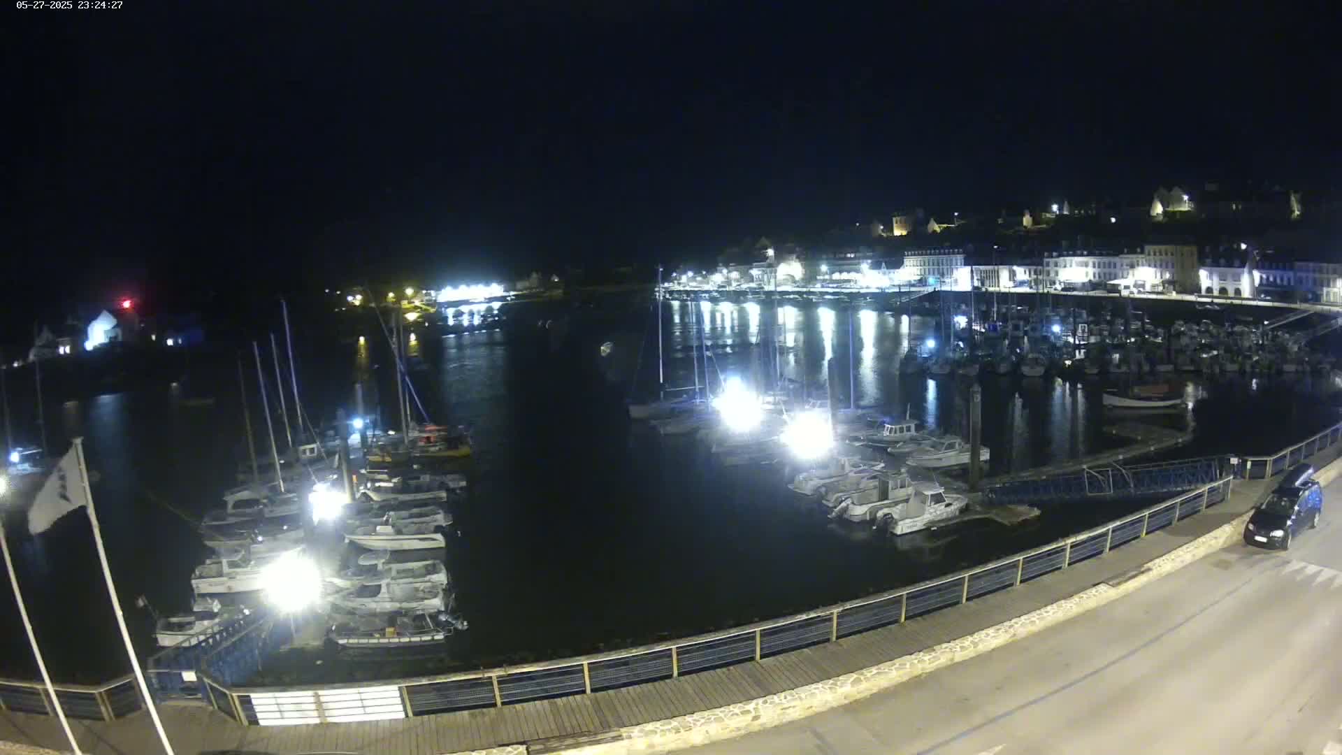 A nighttime view of a harbor filled with boats, with a town's lights reflecting on the dark water.