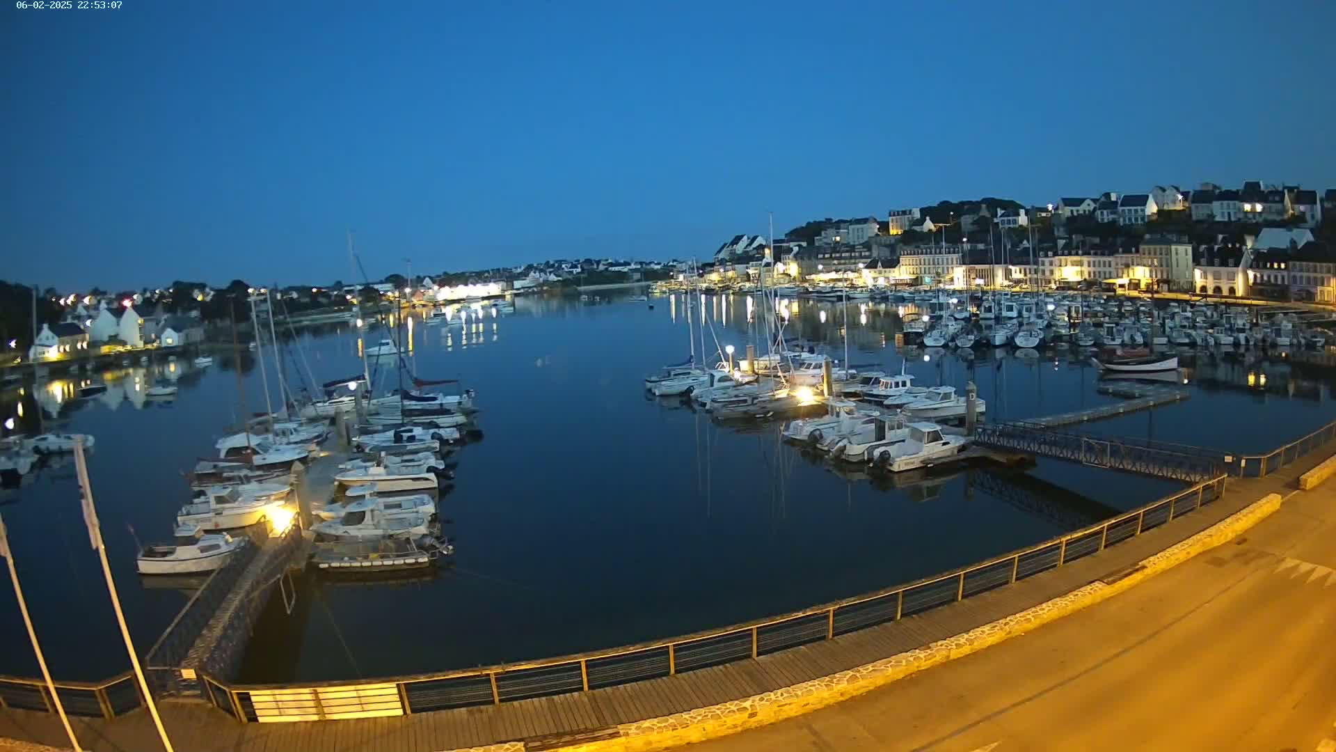 A nighttime view of a harbor filled with boats, next to a town illuminated under a dark blue twilight sky.
