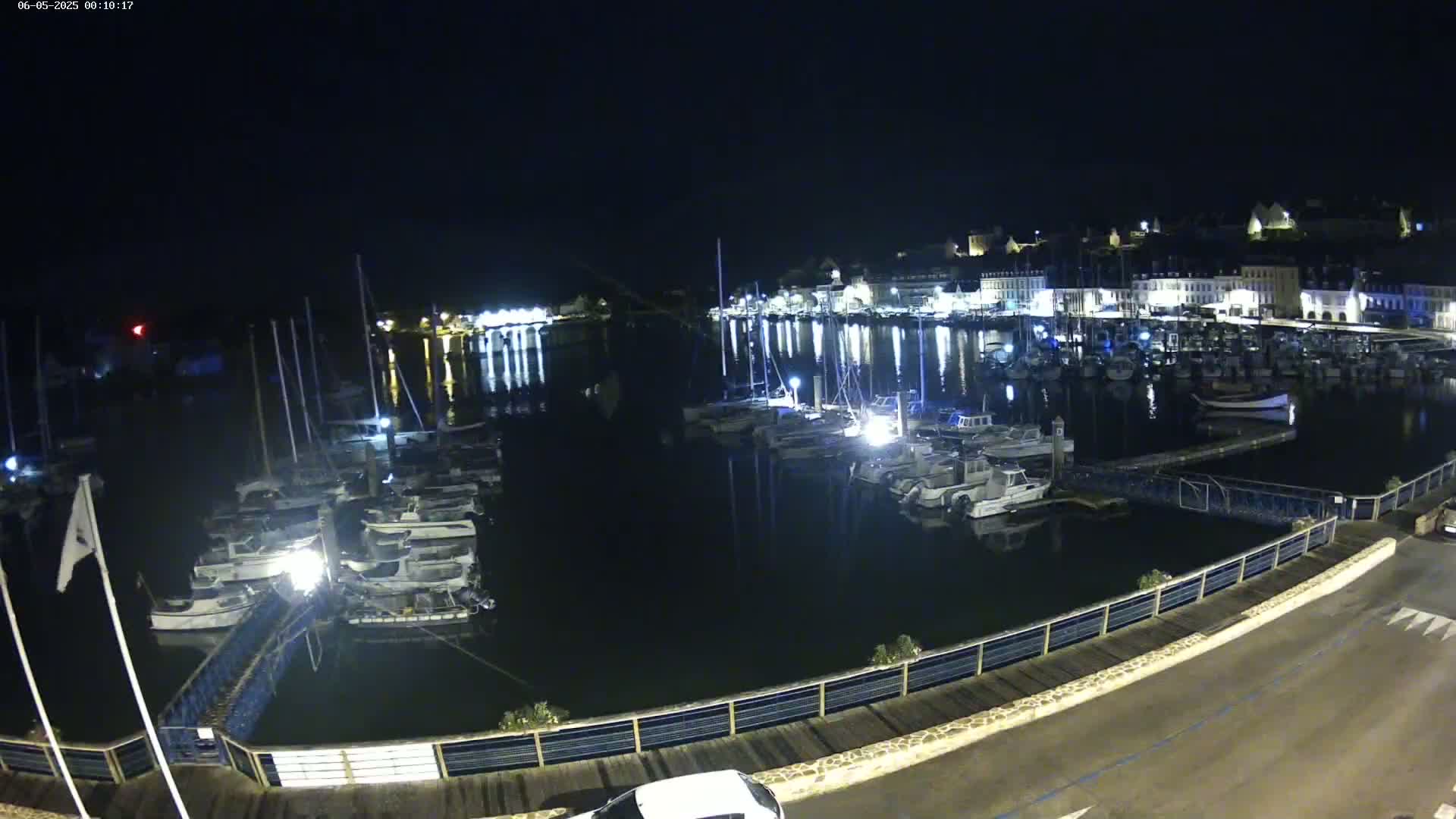 A nighttime view of a harbor filled with boats, reflecting the lights of a town in the background under a dark sky.