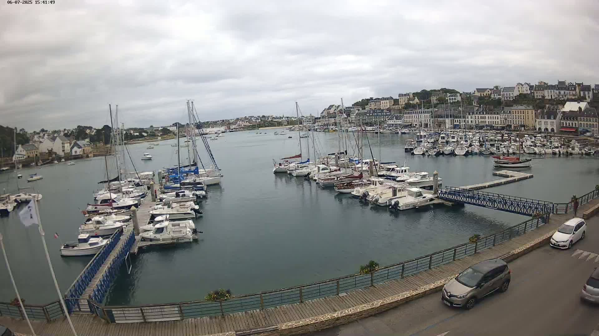 A harbor filled with numerous sailboats and motorboats is situated near a town under an overcast sky.