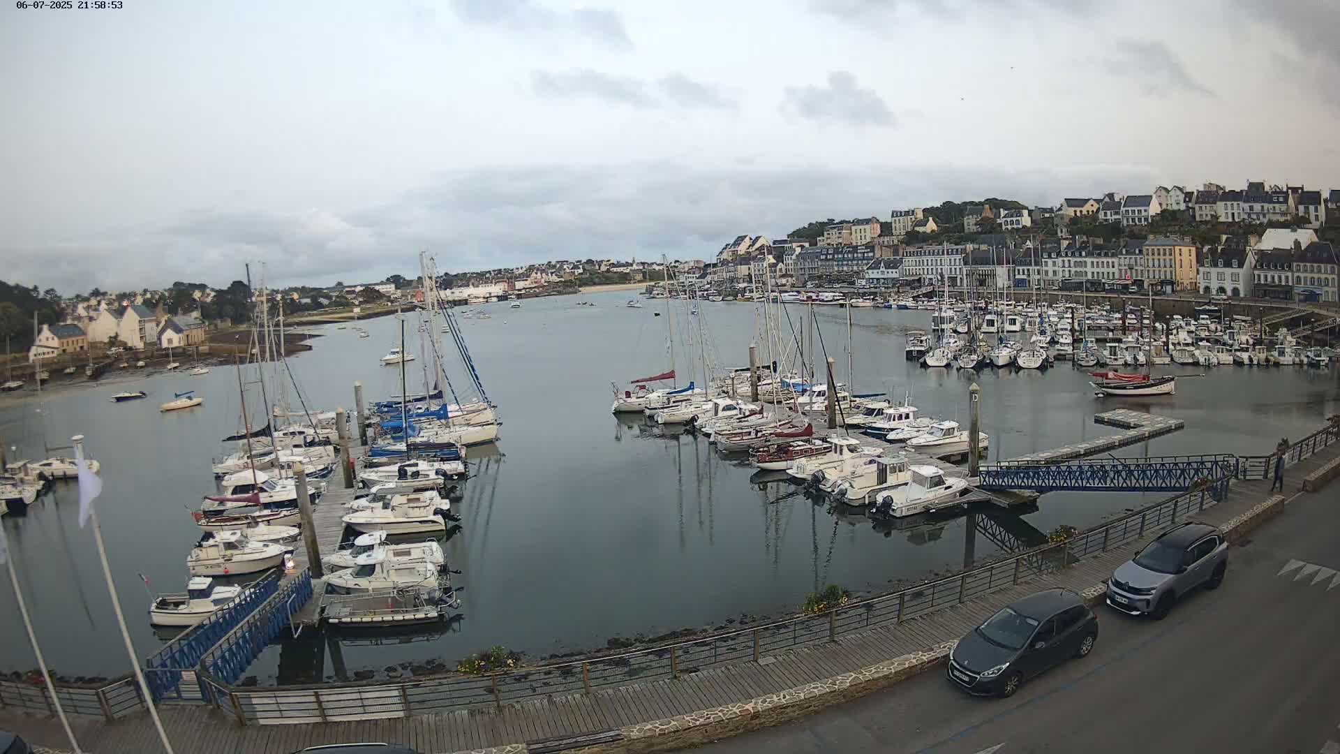 A harbor filled with numerous sailboats and motorboats is situated in front of a town under an overcast sky.