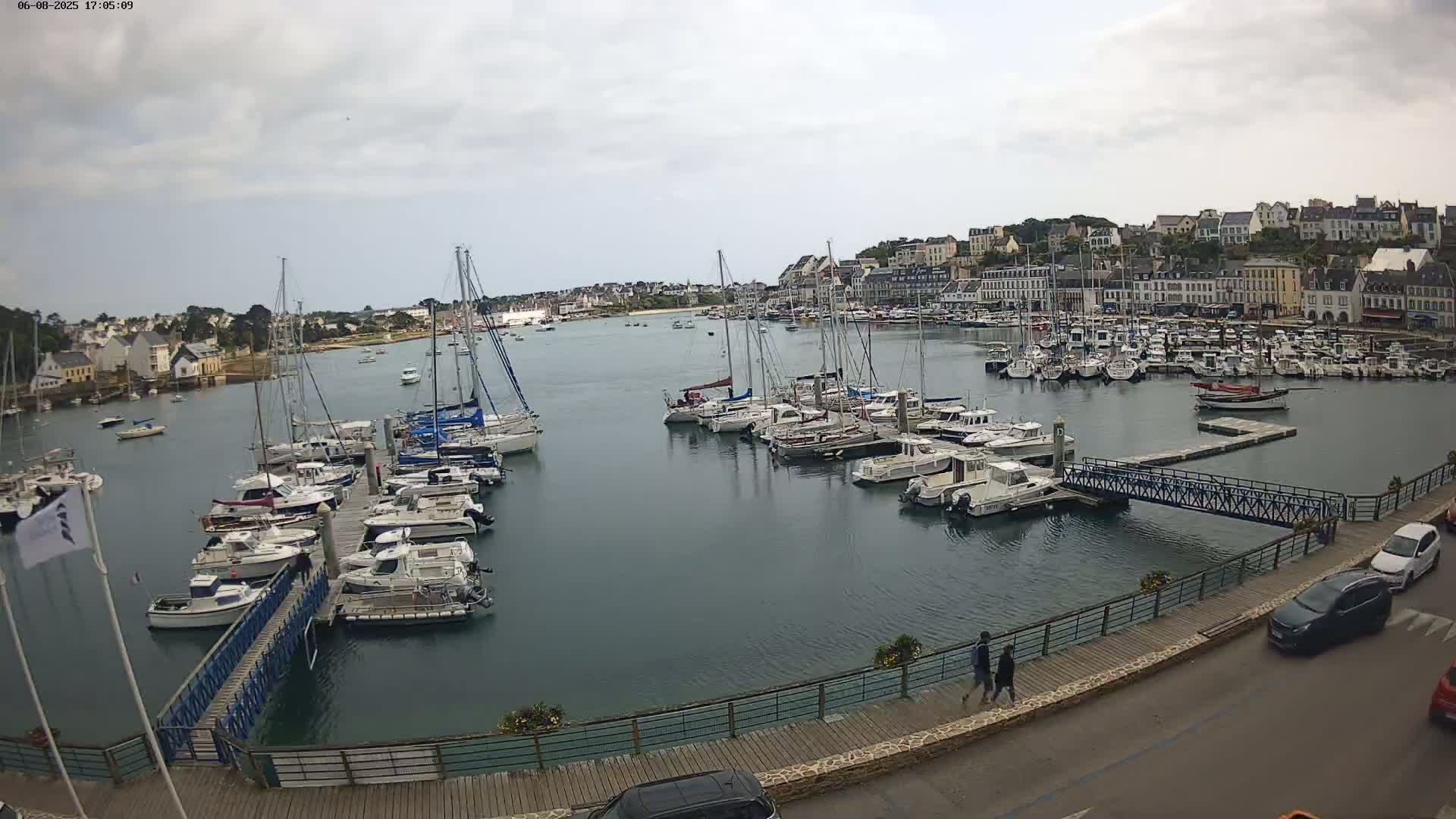 A harbor filled with numerous sailboats and motorboats on a partly cloudy day, with a town visible in the background.
