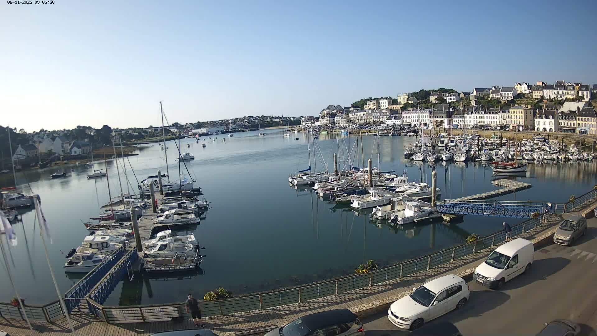 A harbor filled with numerous boats and yachts is situated beside a town of light-colored buildings under a clear, sunny sky.