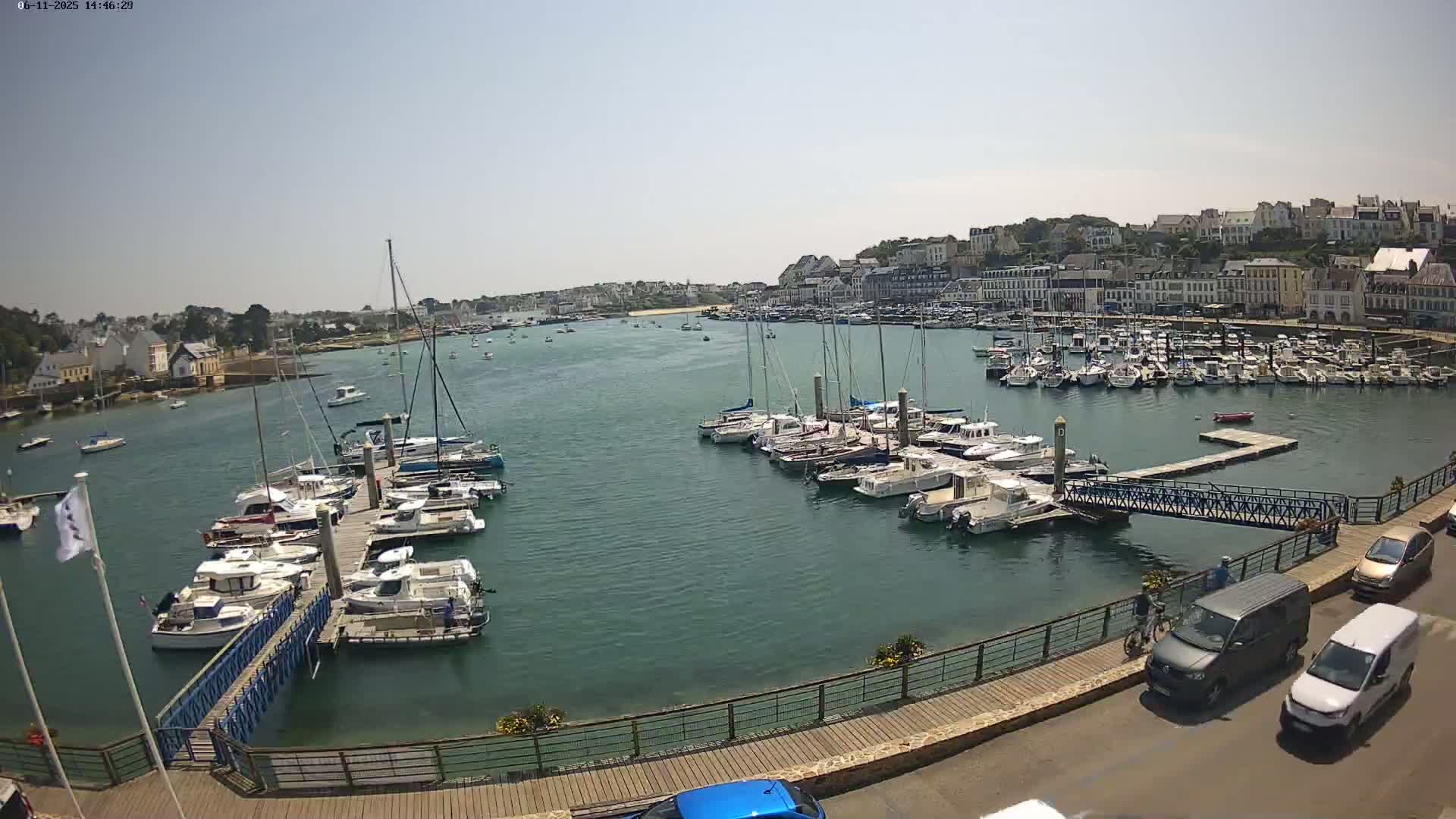 A harbor filled with numerous boats and yachts on a sunny day, with a town visible in the background.