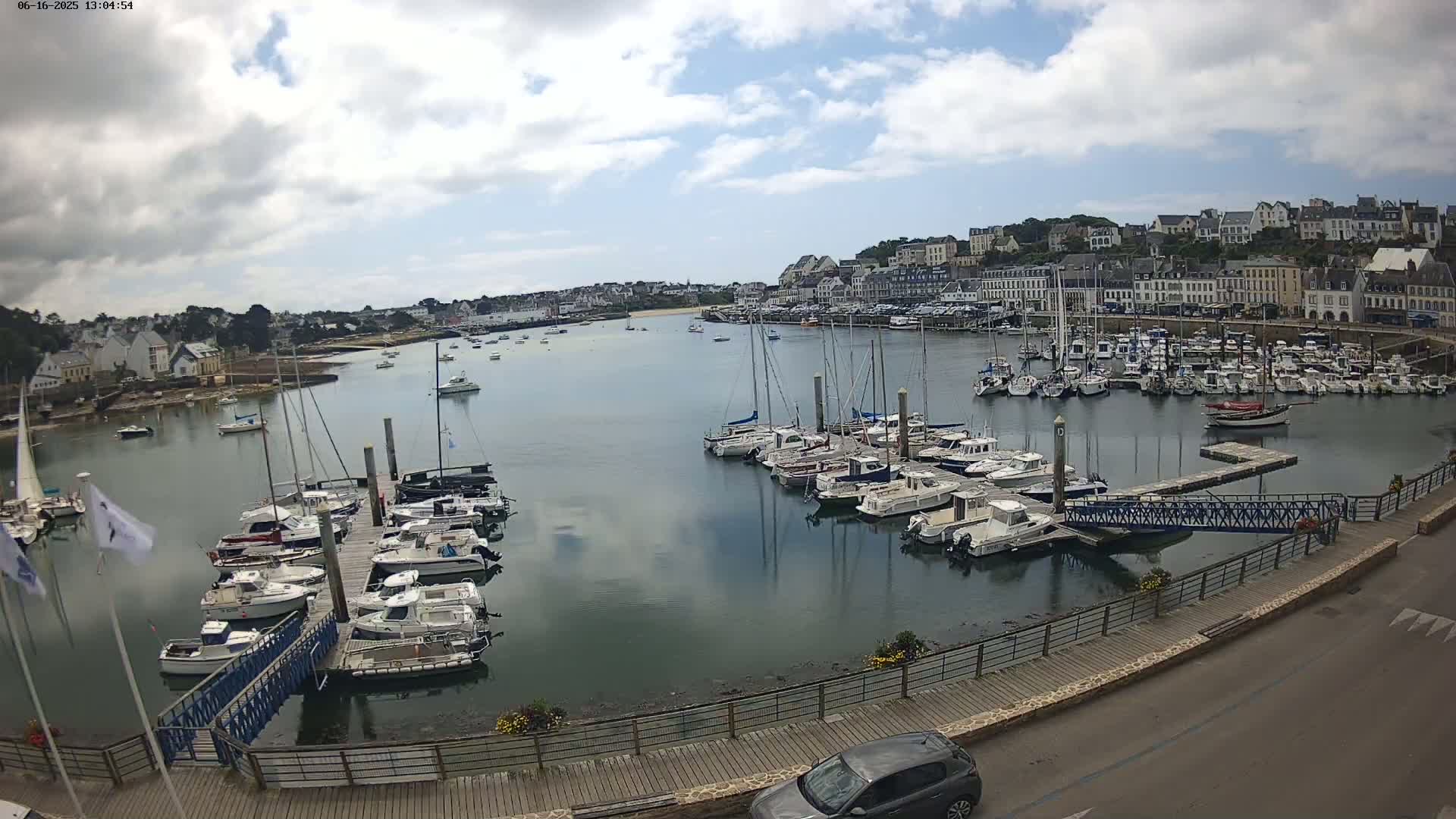 A harbor filled with numerous boats is situated near a town under a partly cloudy sky.