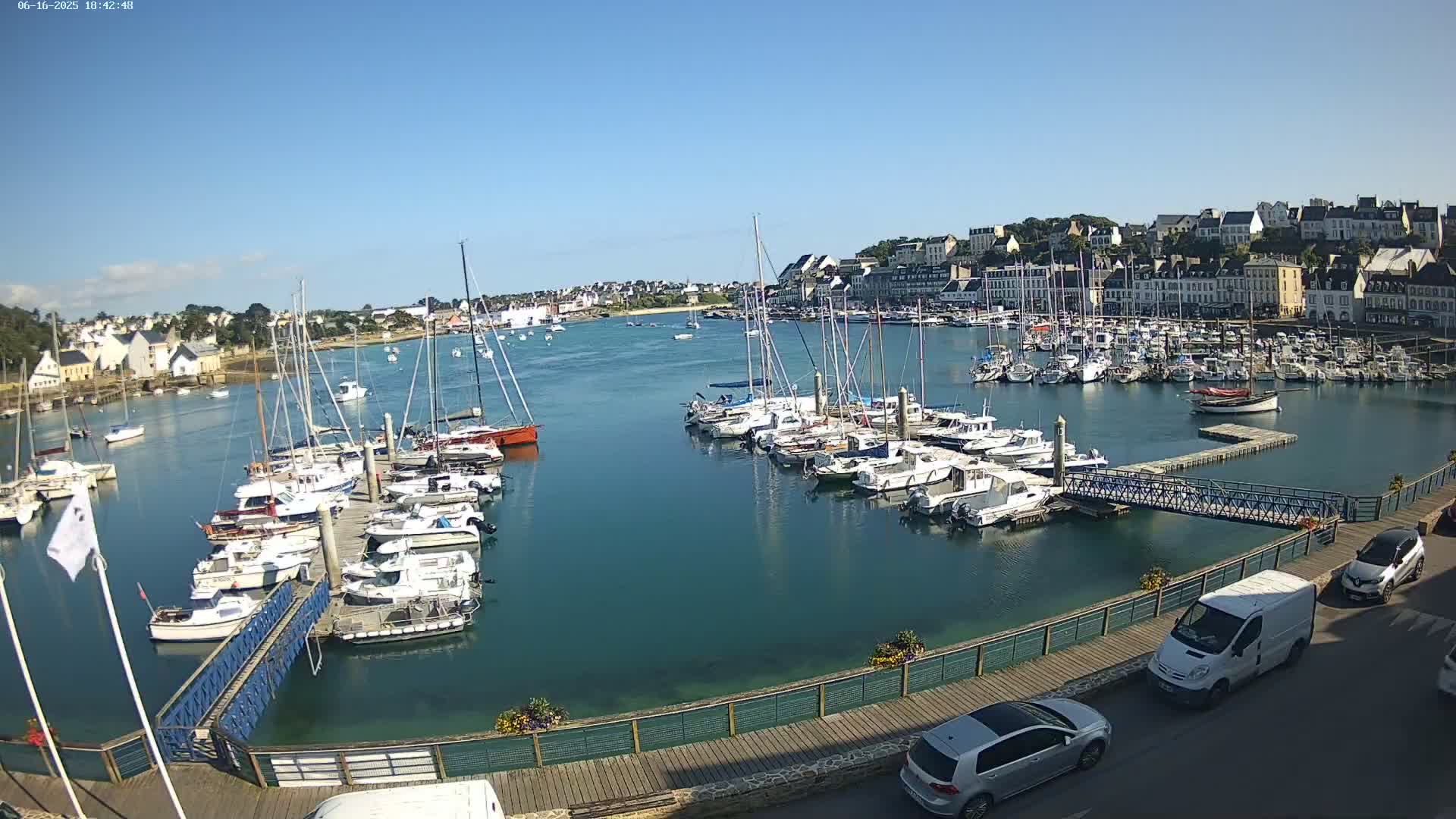 A harbor filled with numerous sailboats and motorboats on a sunny day, with a town visible in the background.
