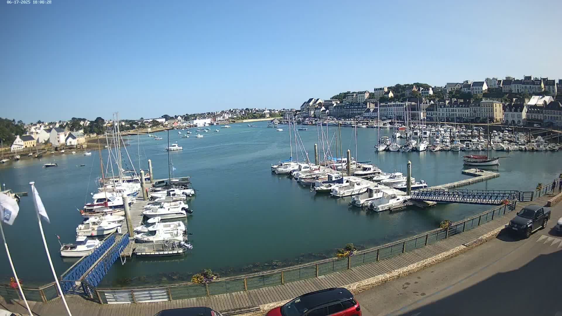 A harbor filled with numerous sailboats and motorboats on a sunny day, with a town visible in the background.