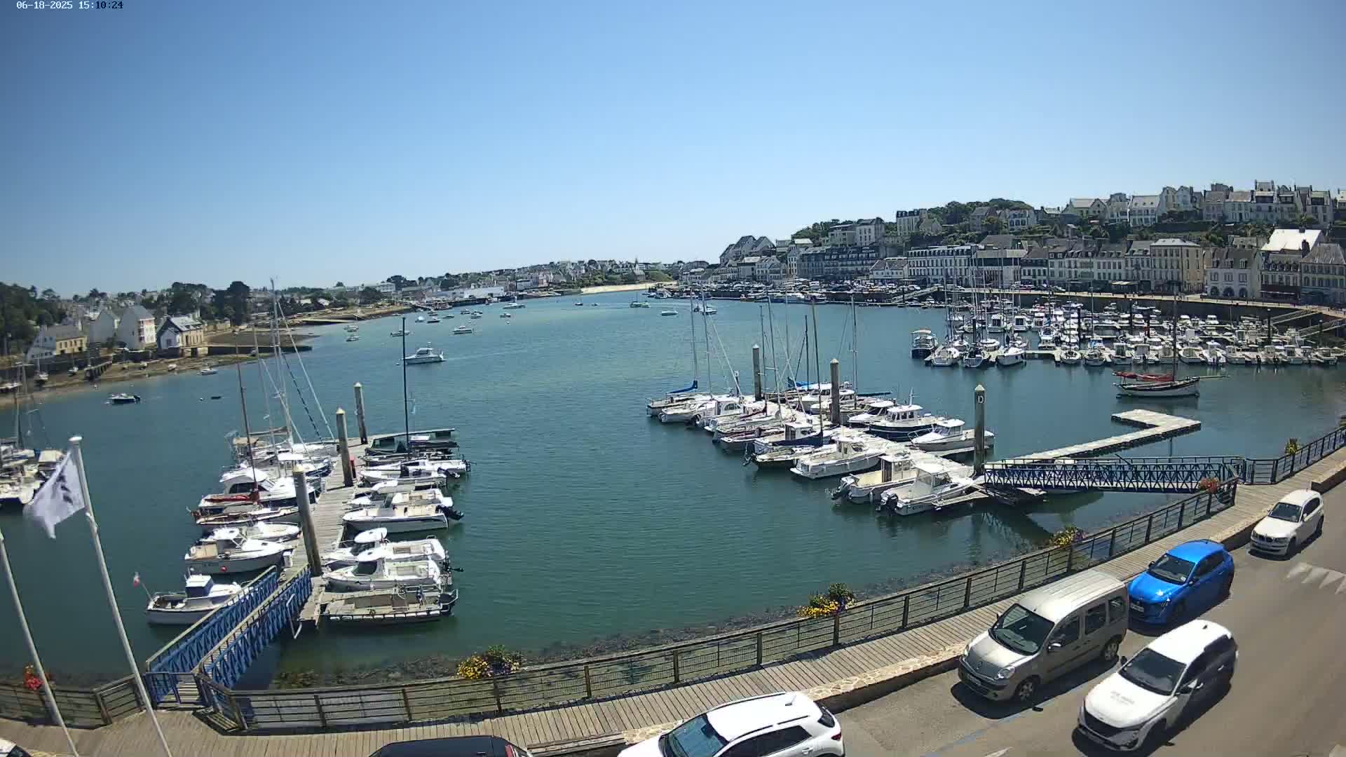 A harbor filled with numerous boats on a sunny day, with a town and buildings visible in the background along a waterfront.