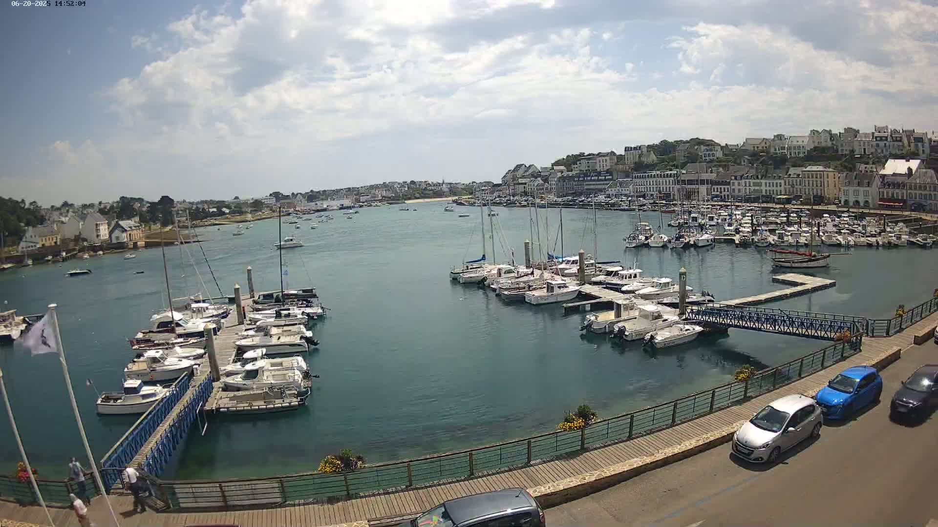 A harbor filled with numerous sailboats and motorboats is situated near a town under a partly cloudy sky.