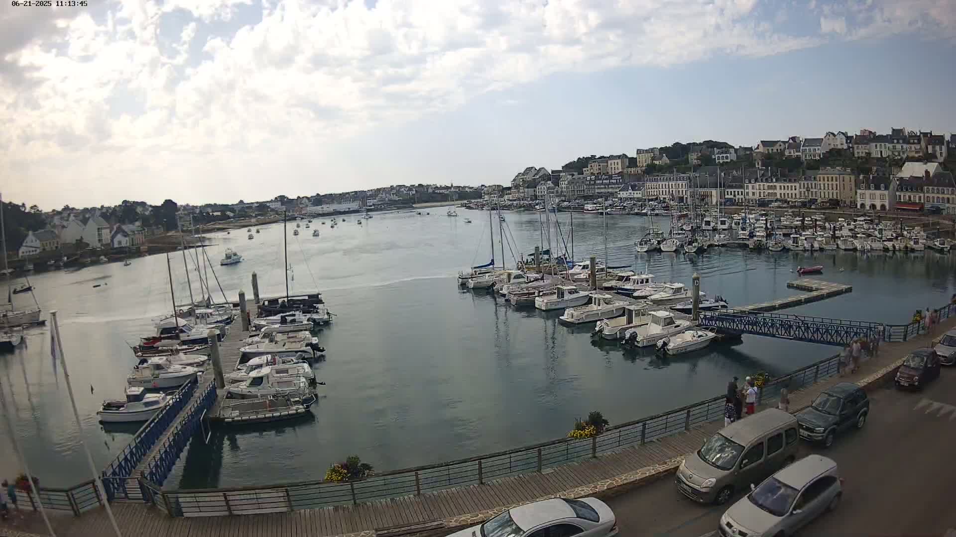 A harbor filled with numerous boats and yachts is situated next to a town under a partly cloudy sky.