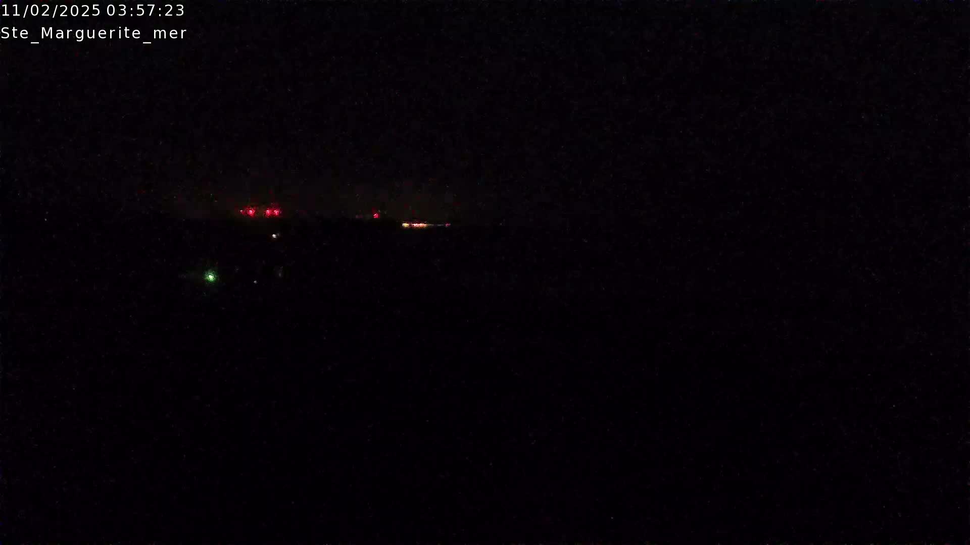 A dark, nighttime scene shows a few distant lights on the horizon under a clear, dark sky.