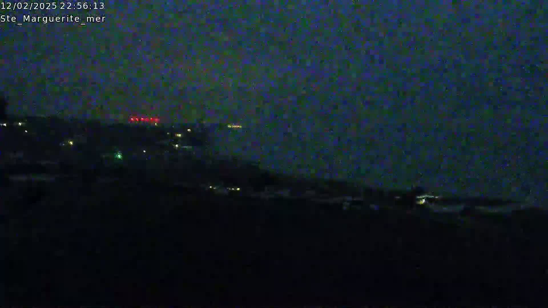 A nighttime long shot shows a dark landscape with scattered lights in the distance, under a dark, possibly cloudy sky.
