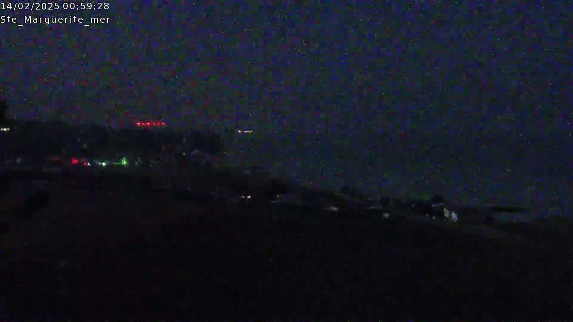 A dark, nighttime scene shows a distant, dimly lit shoreline with scattered lights under a dark sky.
