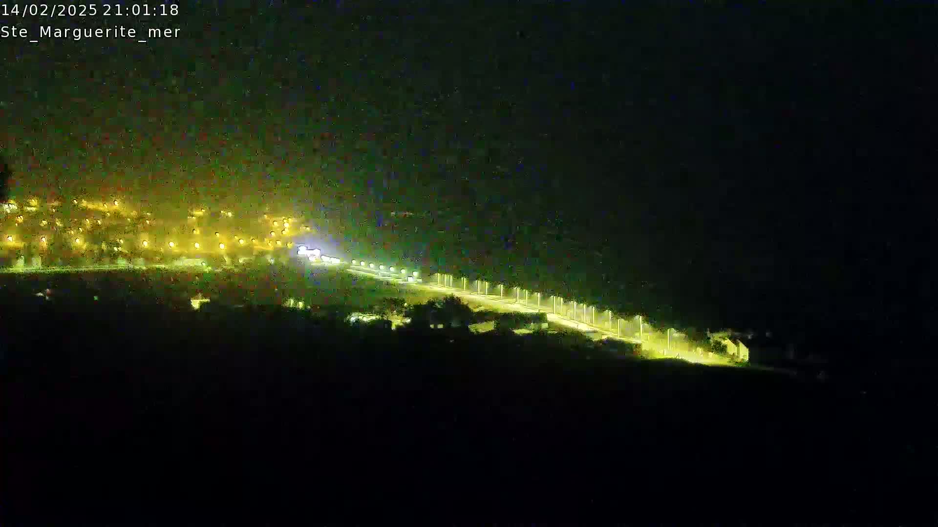 A brightly lit road stretches from a town with numerous lights into the dark night.