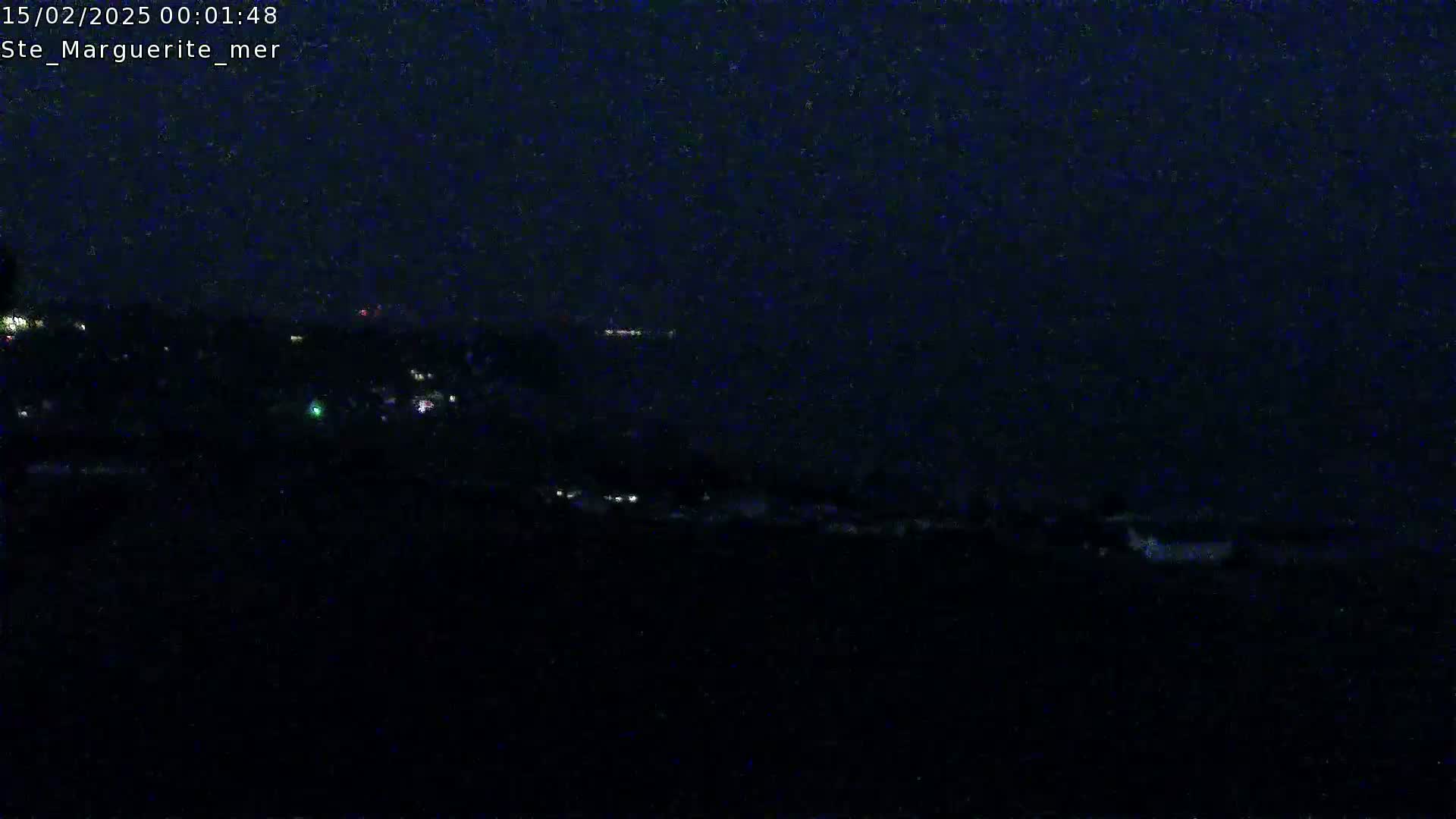 A nighttime, dark view of a distant coastline with scattered lights visible under a seemingly clear sky.