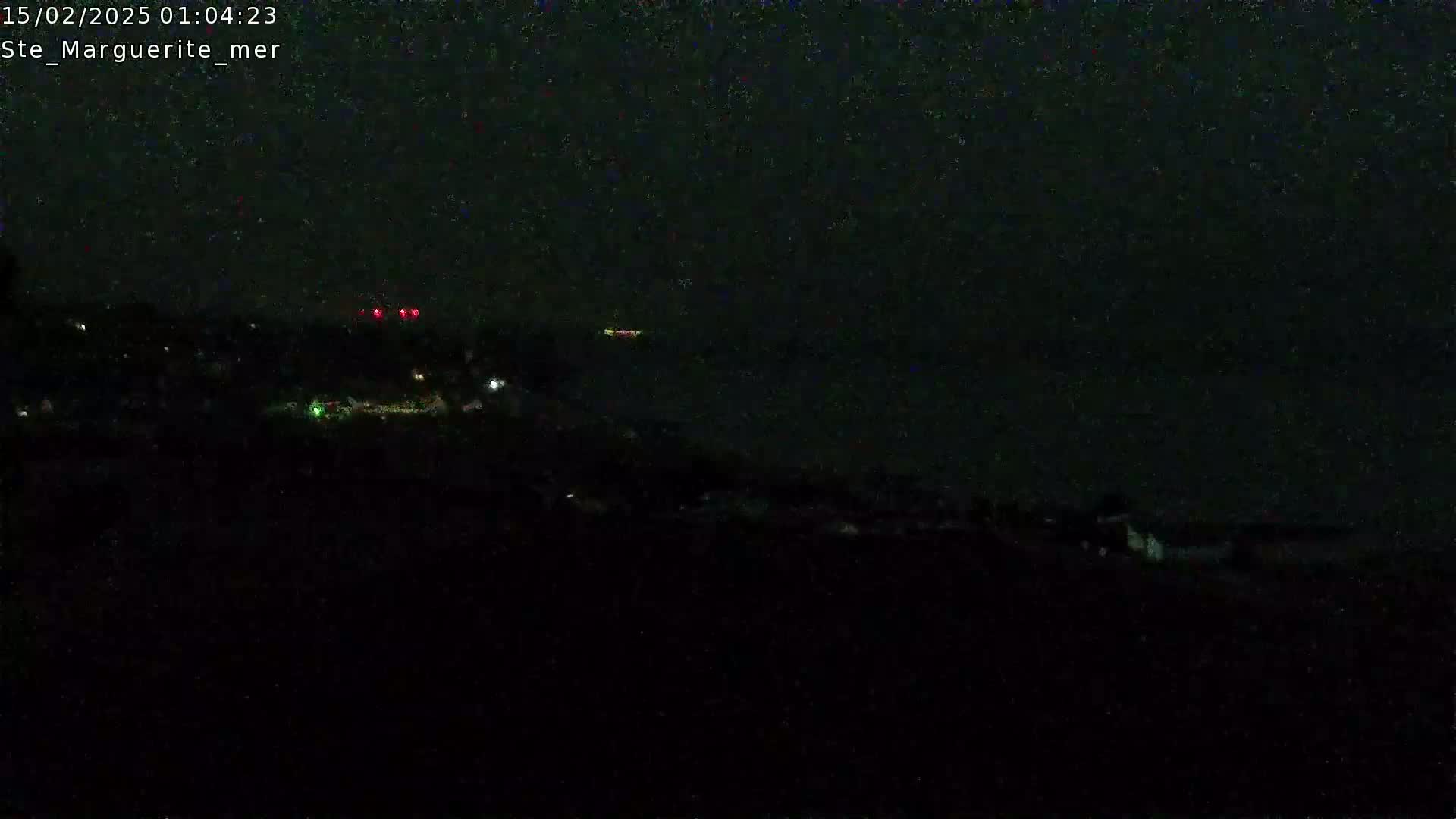 A dark nighttime scene shows a body of water with a few distant lights, and a dark shoreline with a few scattered lights.