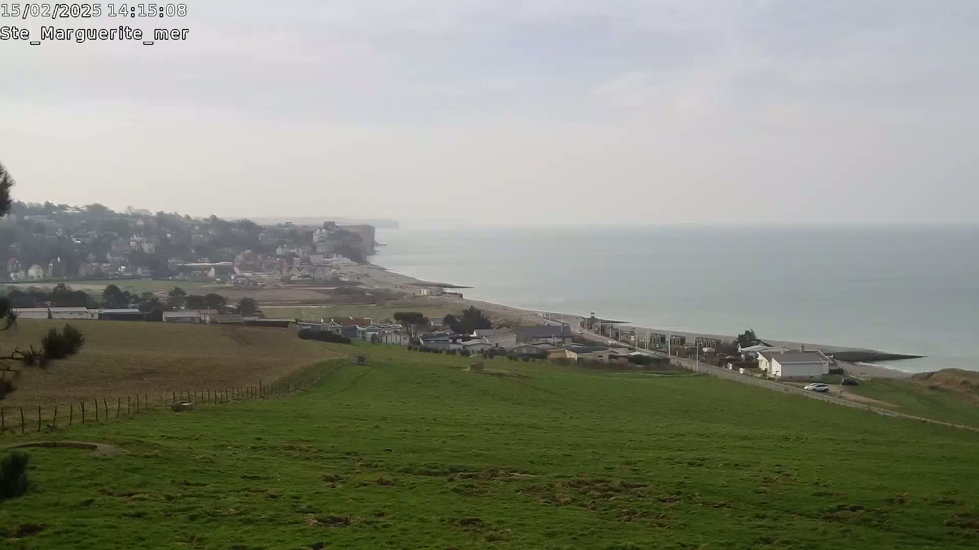 A view from a grassy hill overlooking a coastal town and a calm sea under an overcast sky.