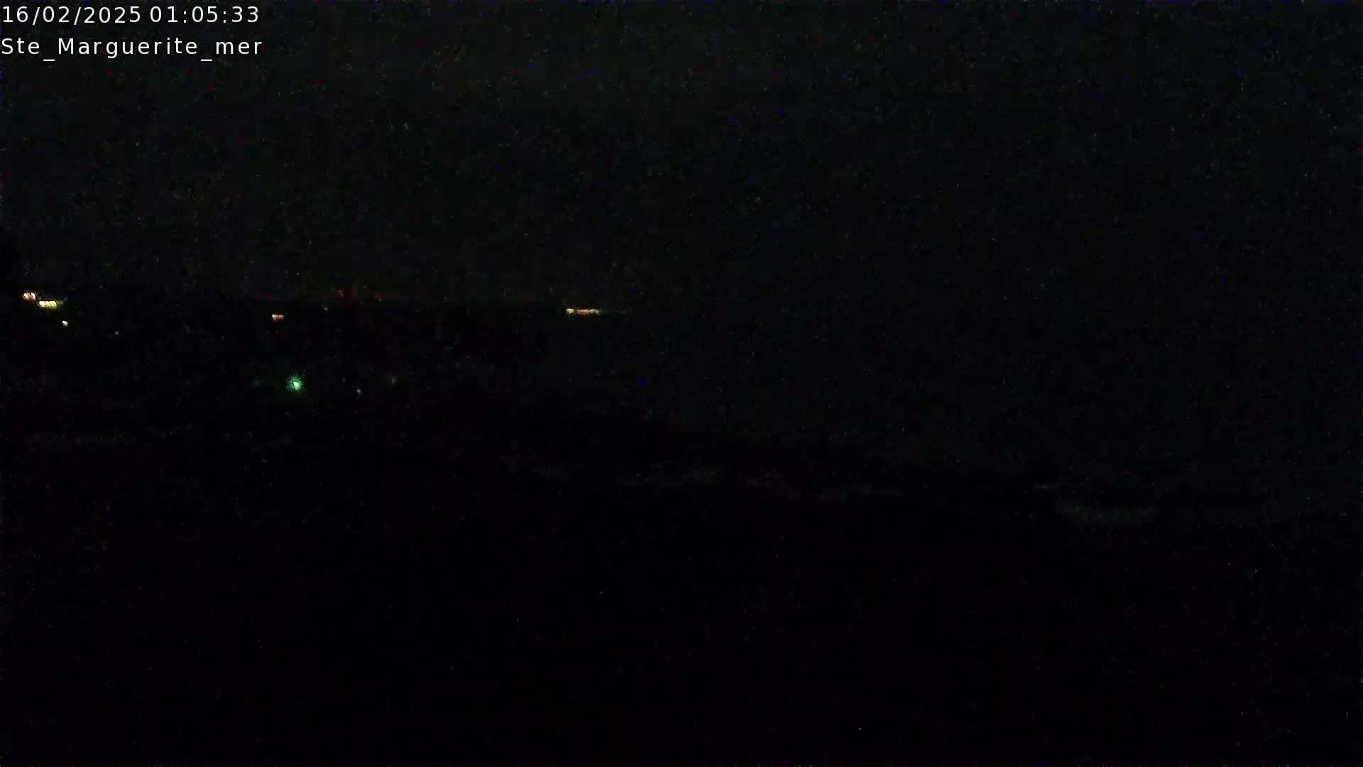 A dark nighttime scene shows a distant, faint horizon line with a few small, scattered lights visible against a completely black sky.