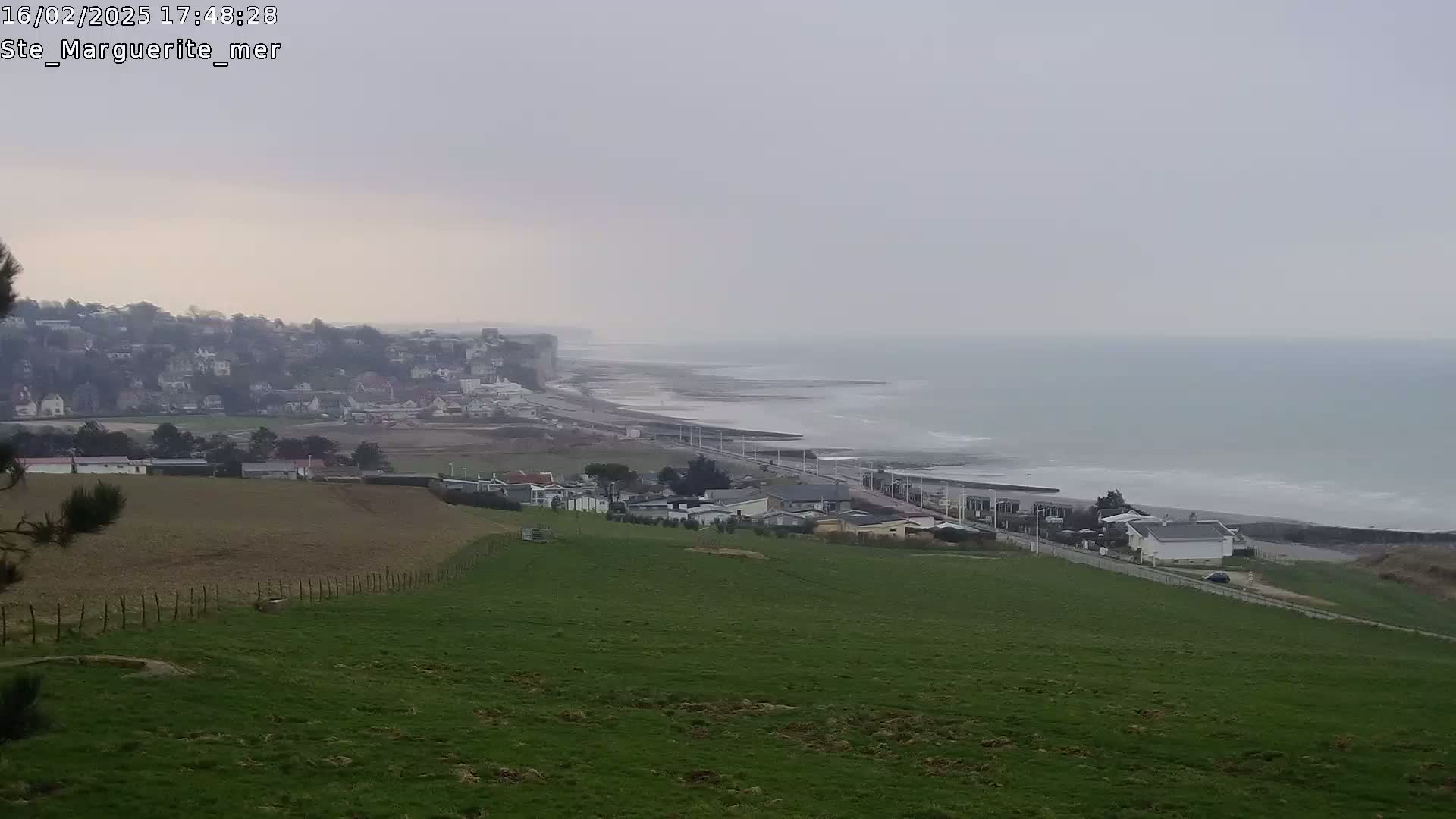 A coastal town sits on a cliff overlooking a grayish-blue sea under an overcast sky.
