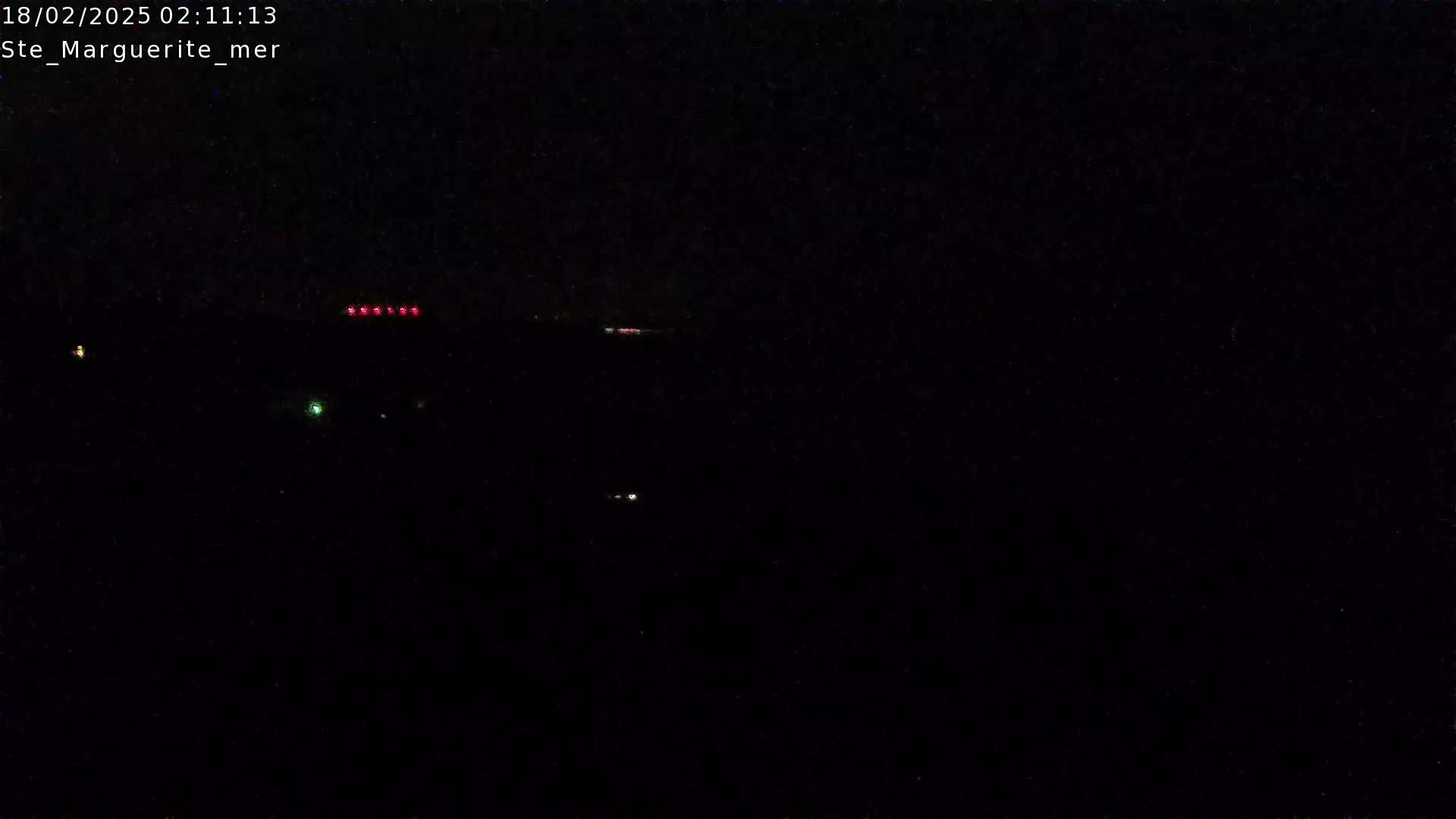 A nighttime, dark scene shows a few distant lights, possibly from ships or vehicles.