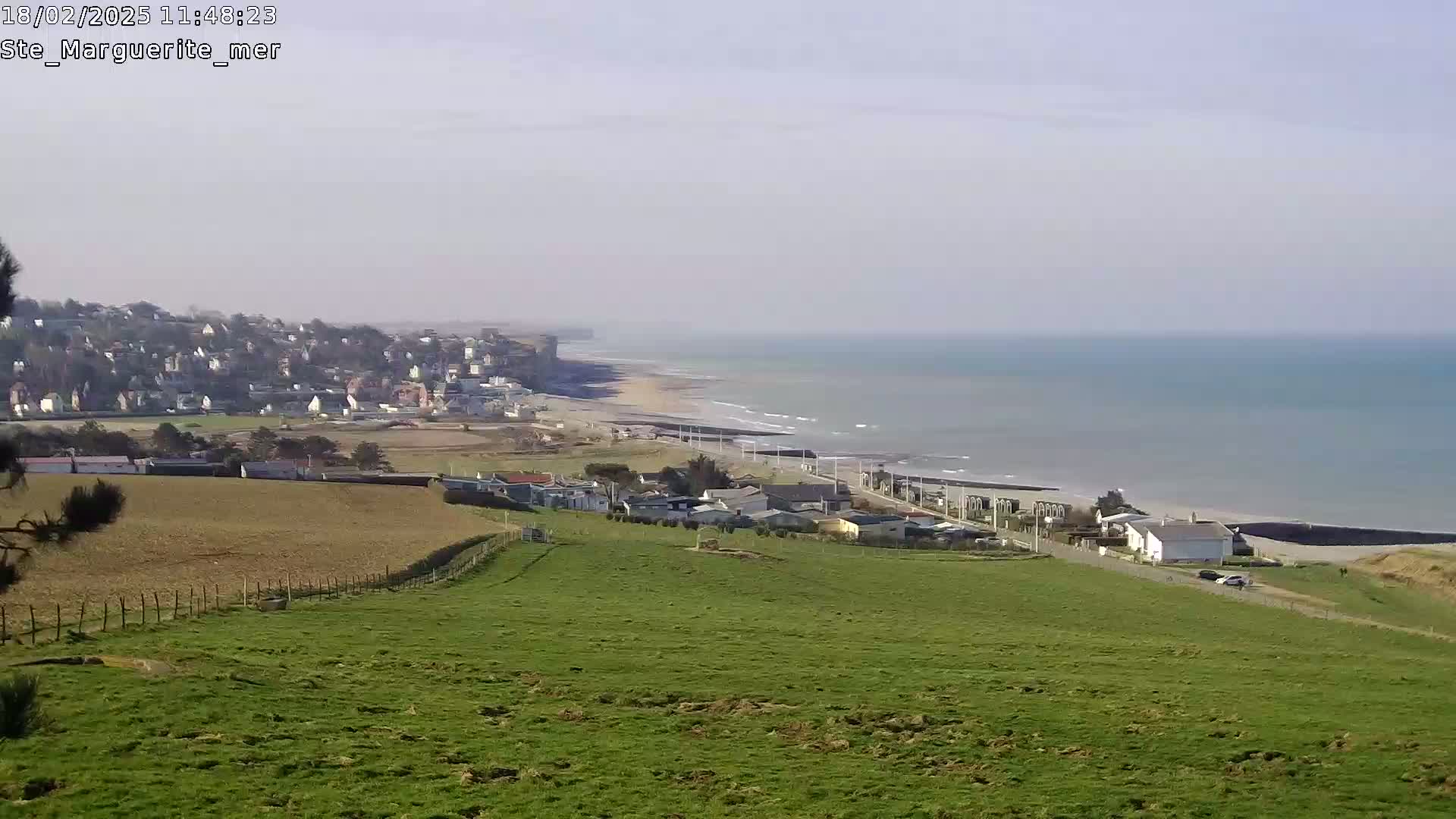 A coastal town is visible in the distance, situated alongside a sandy beach and a calm ocean under a clear sky.