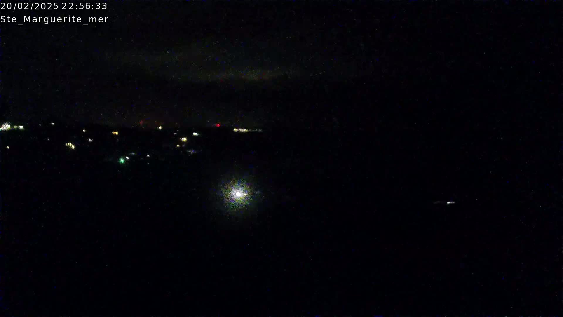 A nighttime, long-distance view shows a scattering of small, distant lights, possibly from a town or village, under a dark, cloudy sky.