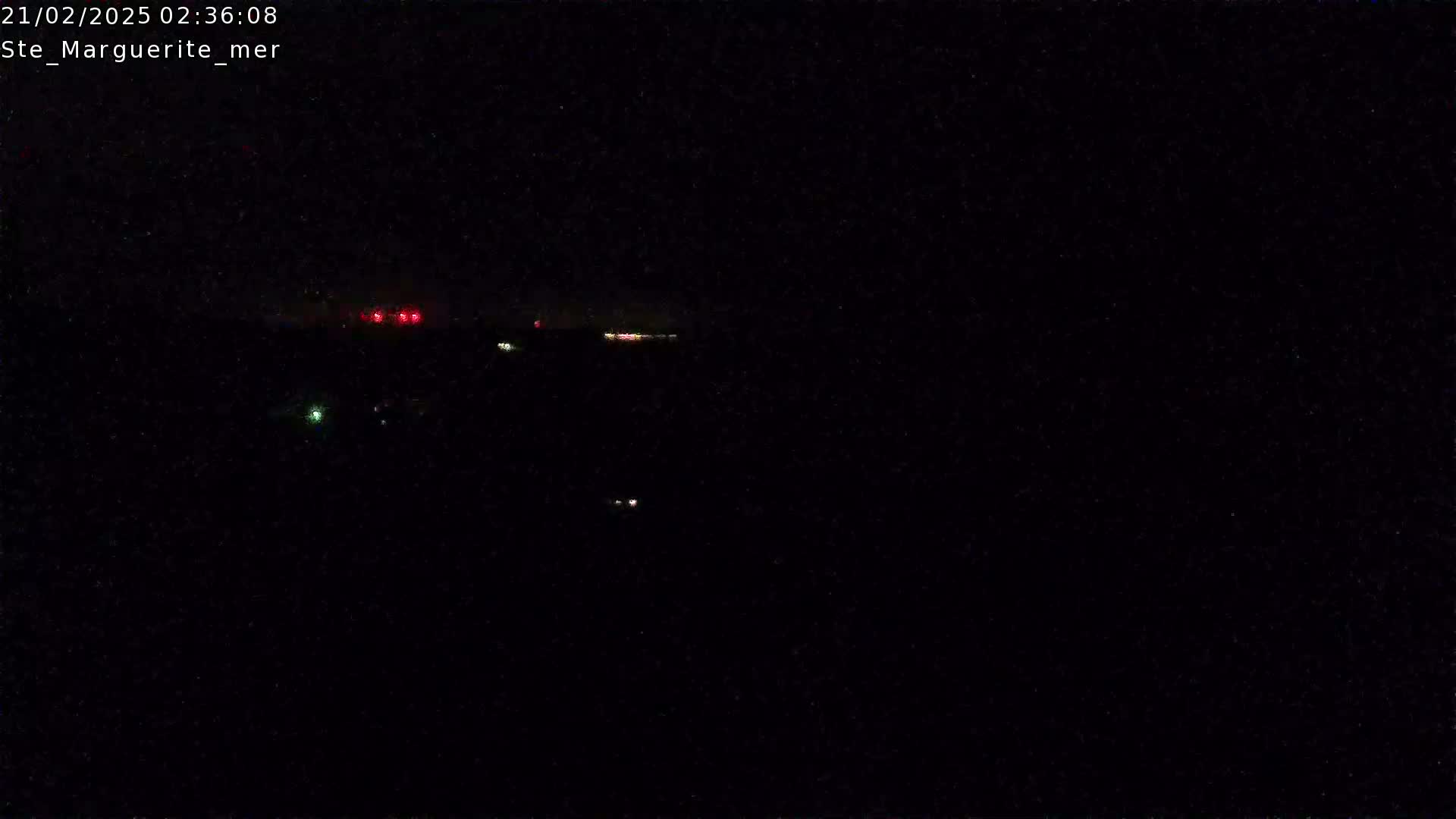 A nighttime, dark image shows a few faint red and green lights in the distance.