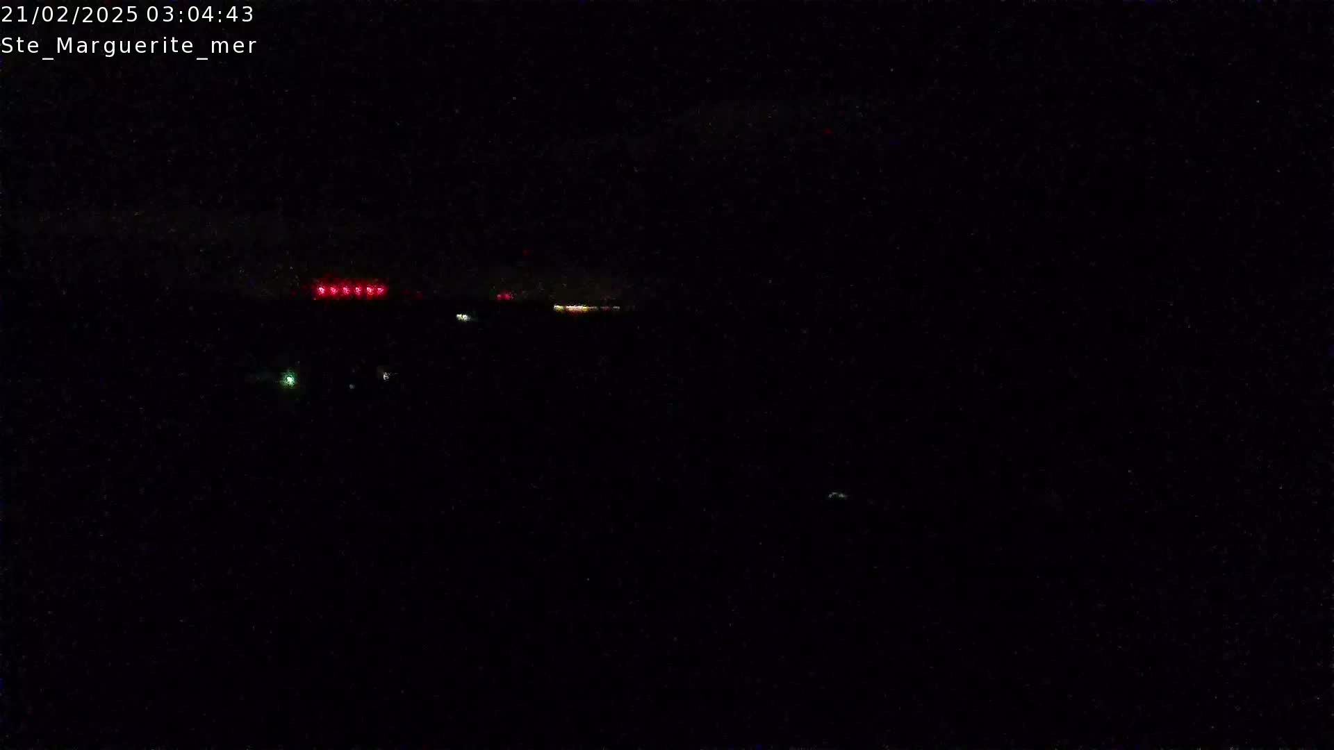 A nighttime, dark image shows a few distant red and amber lights on a dark horizon.