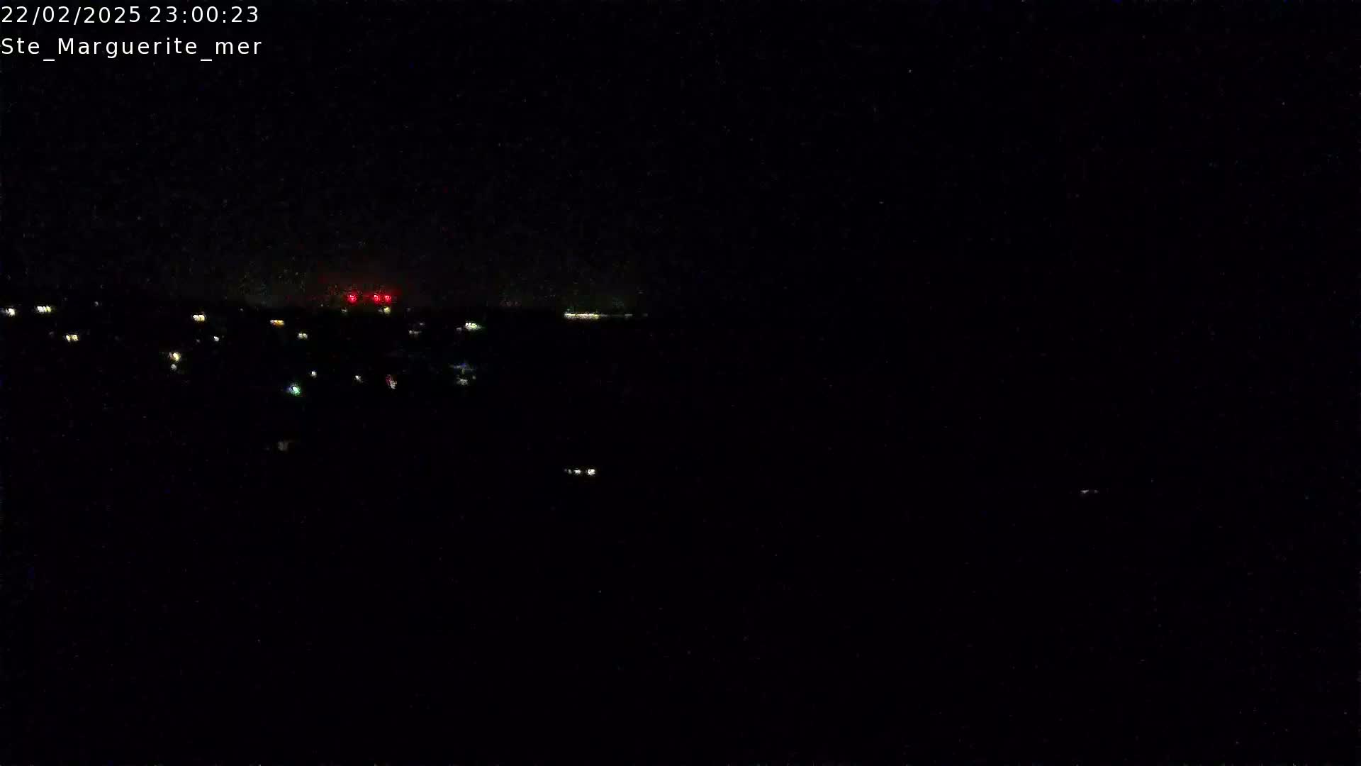 A nighttime long shot shows a dark landscape with a few distant lights and a faint horizon line under a clear, dark sky.