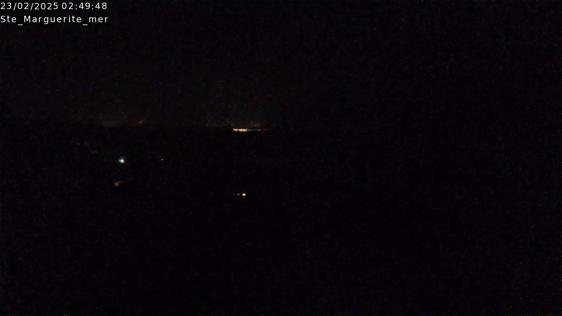 A dark, nighttime scene shows a few faint lights in the distance under a clear, dark sky.