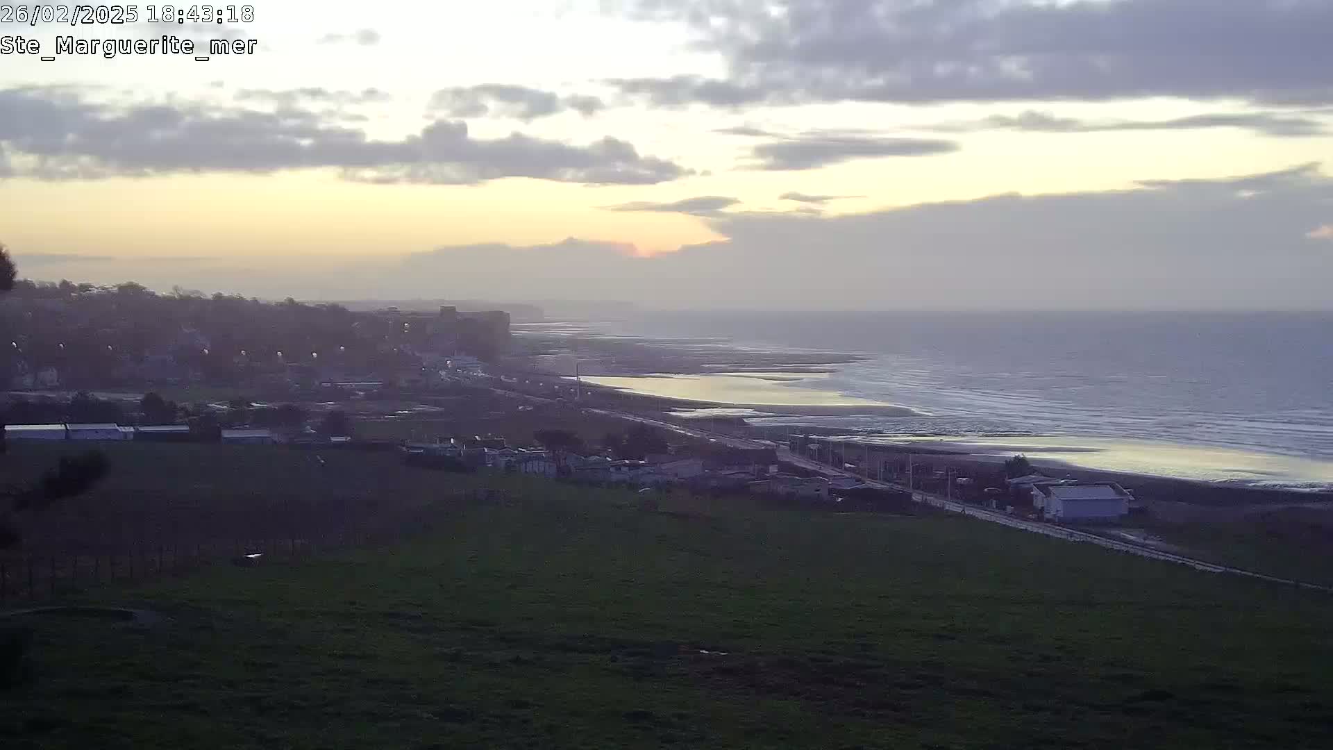 A coastal town at sunset, with a calm ocean and overcast sky.