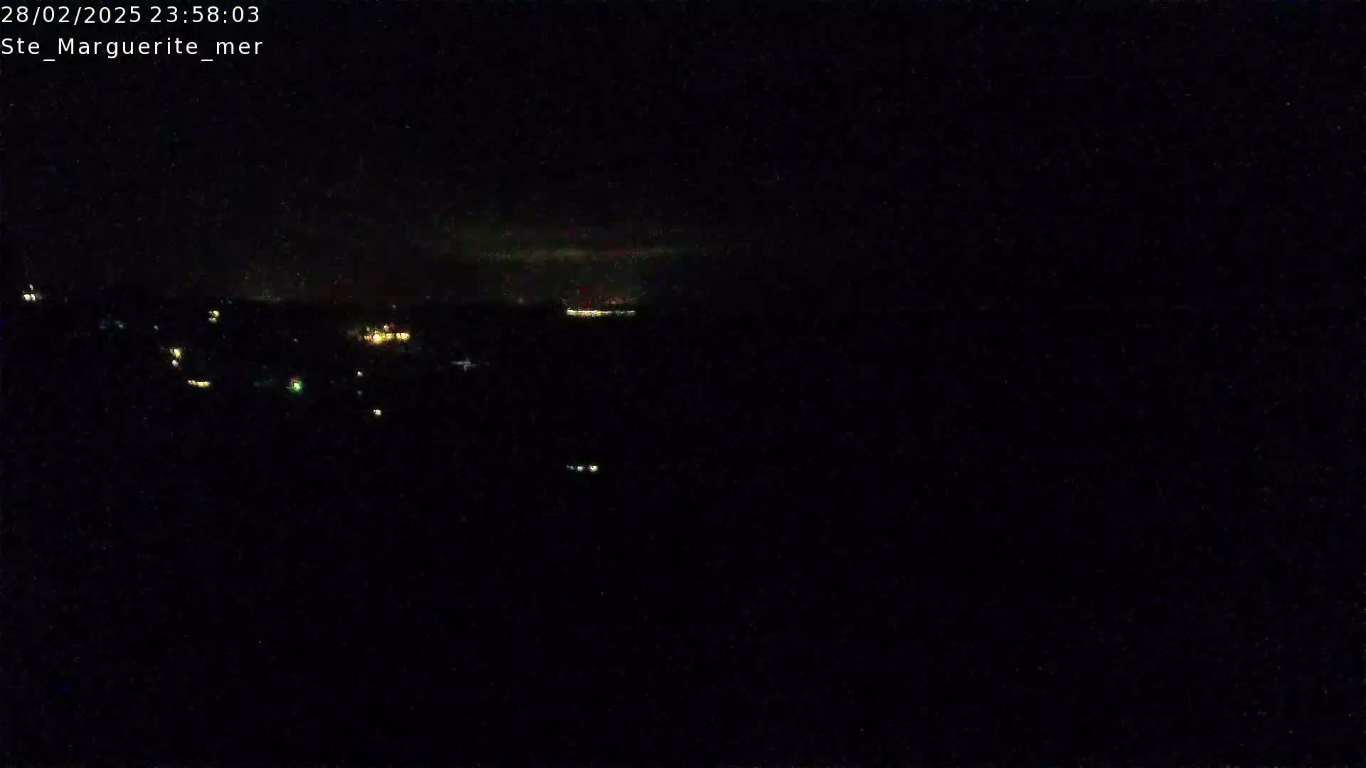 A nighttime, dark, outdoor scene shows a distant line of faint lights possibly indicating a town or city under a cloudy sky.