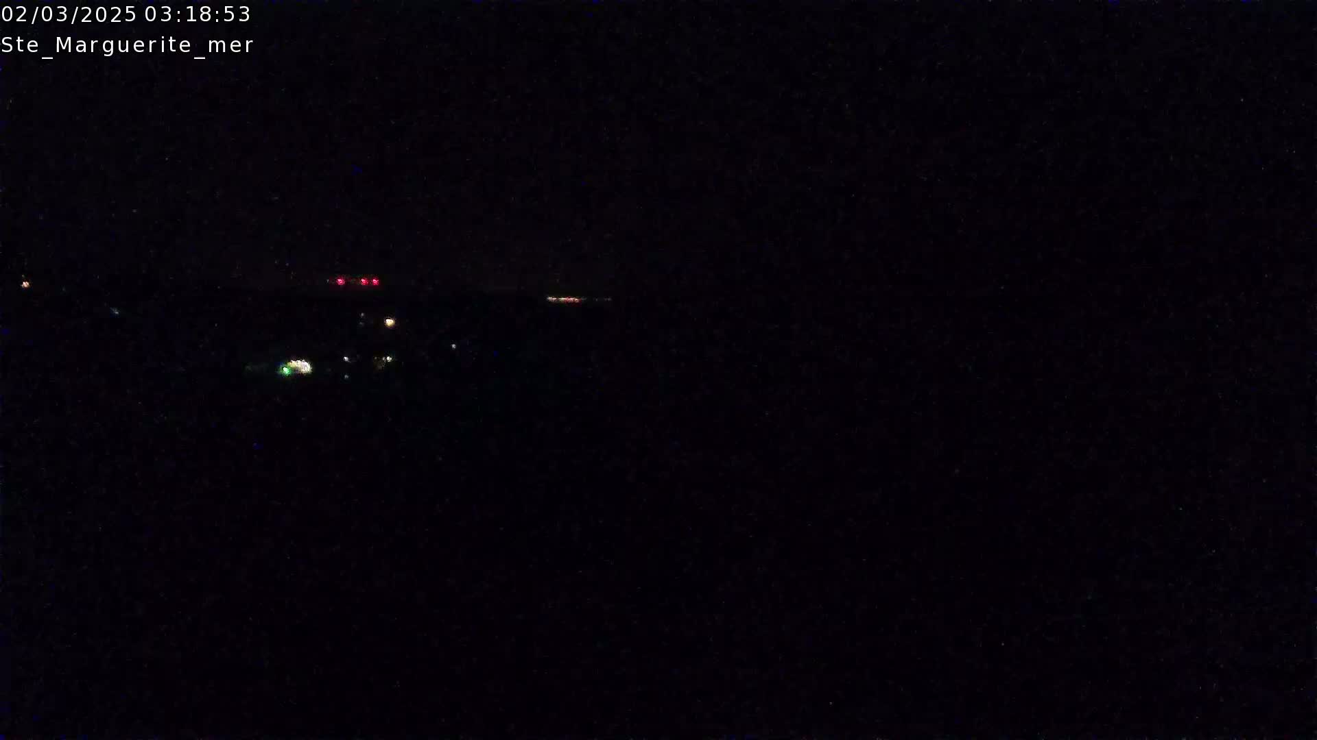 A dark, nighttime scene shows a few distant lights on the horizon under a clear, black sky.