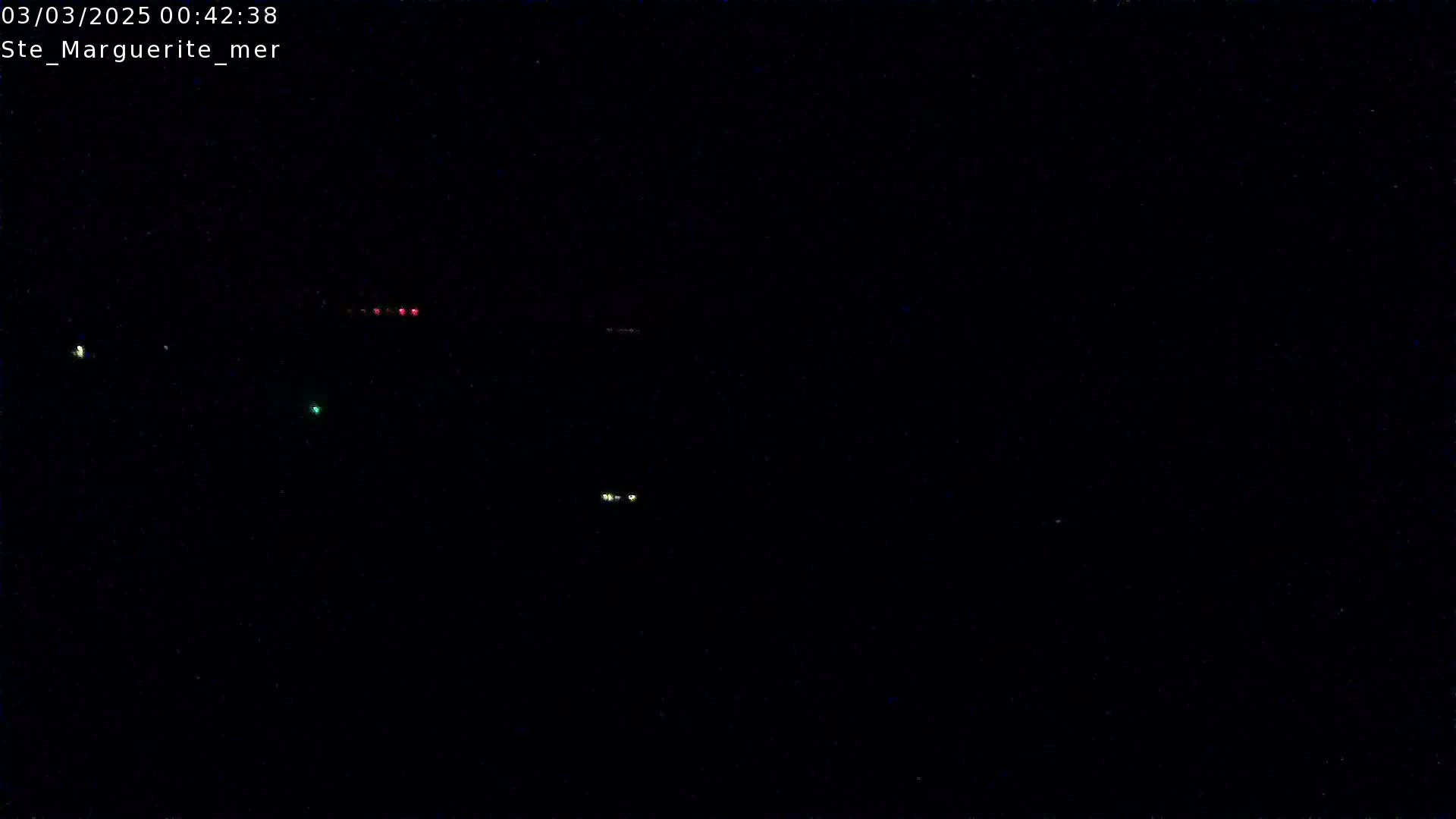 A nighttime image shows several faint lights in the distance against a completely dark background.