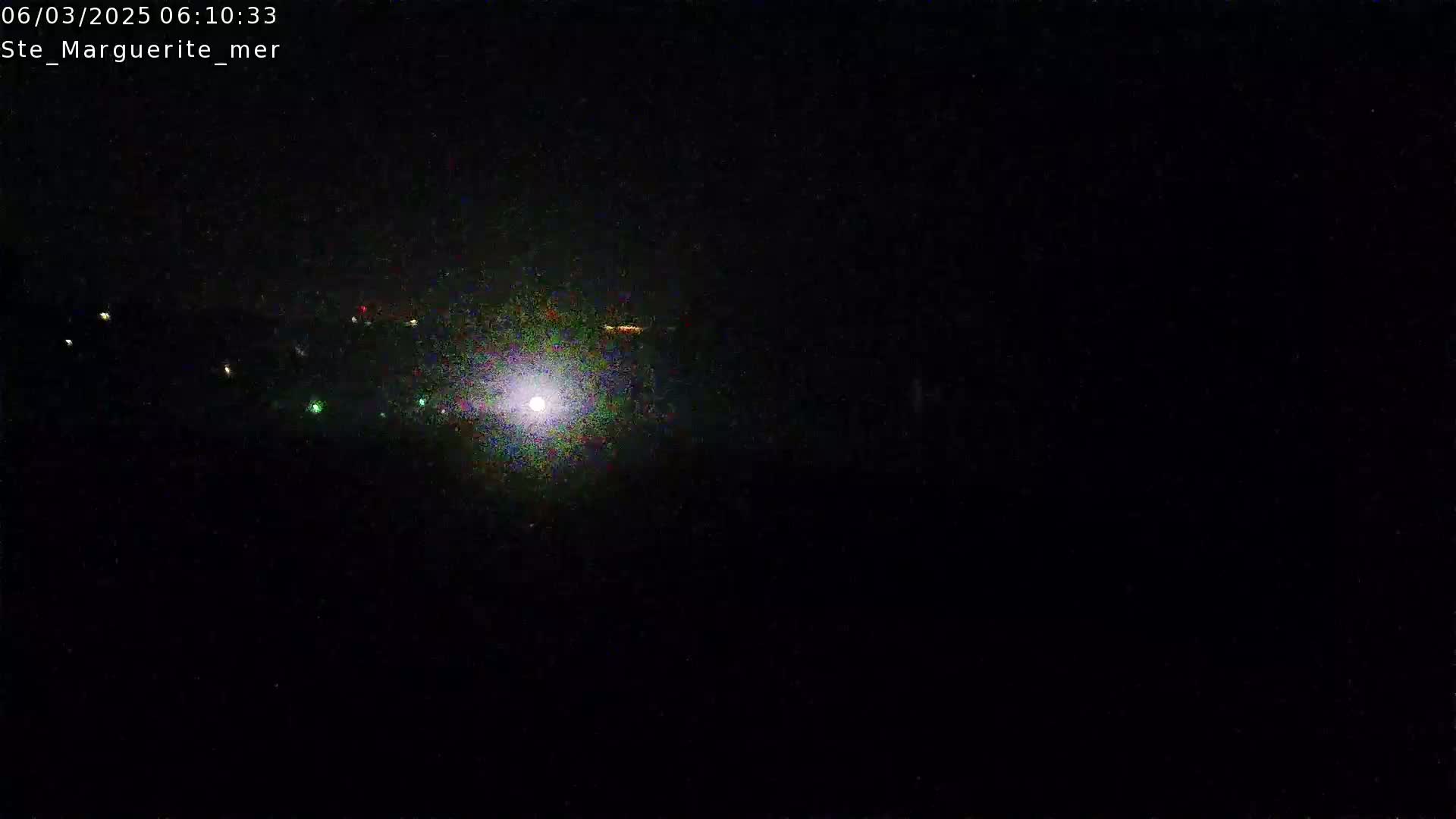 A nighttime, low-light image shows a bright light source in the center and several fainter lights scattered across the dark foreground.