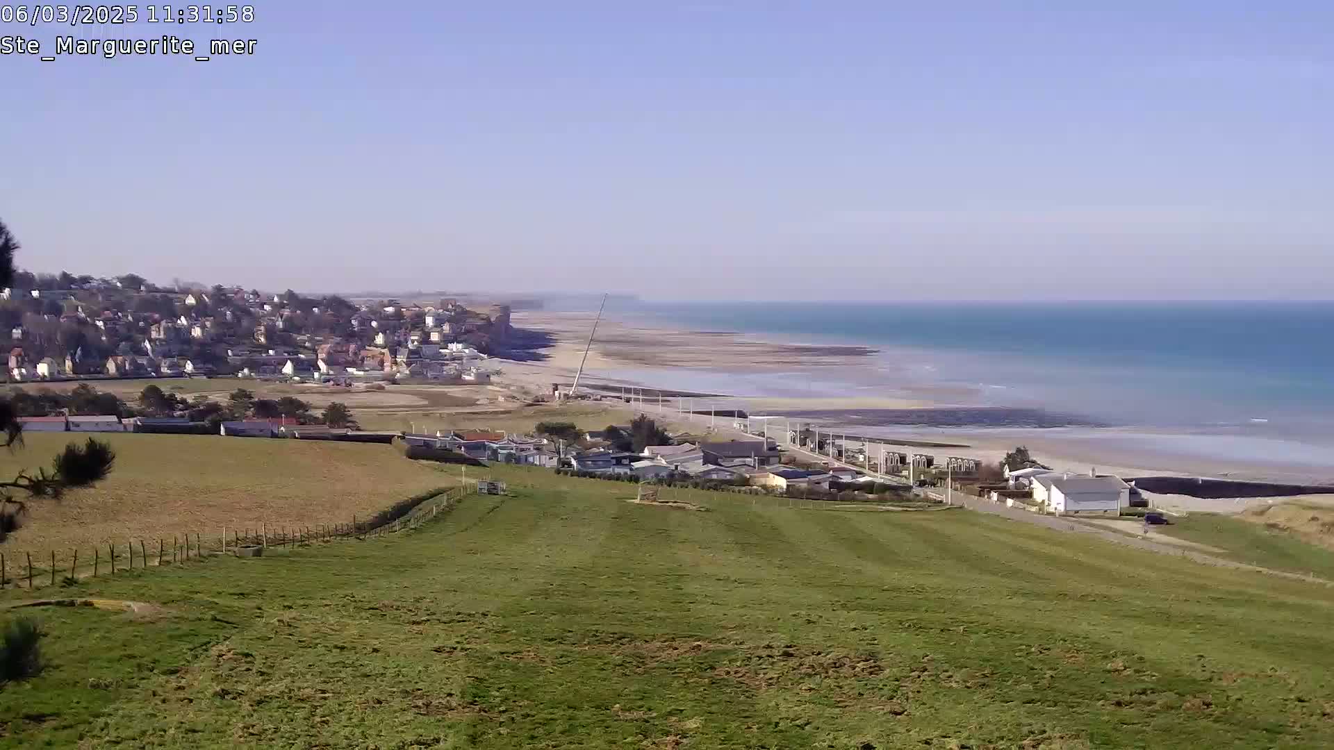 A coastal town nestled beside a long, sandy beach and calm turquoise ocean under a clear blue sky.