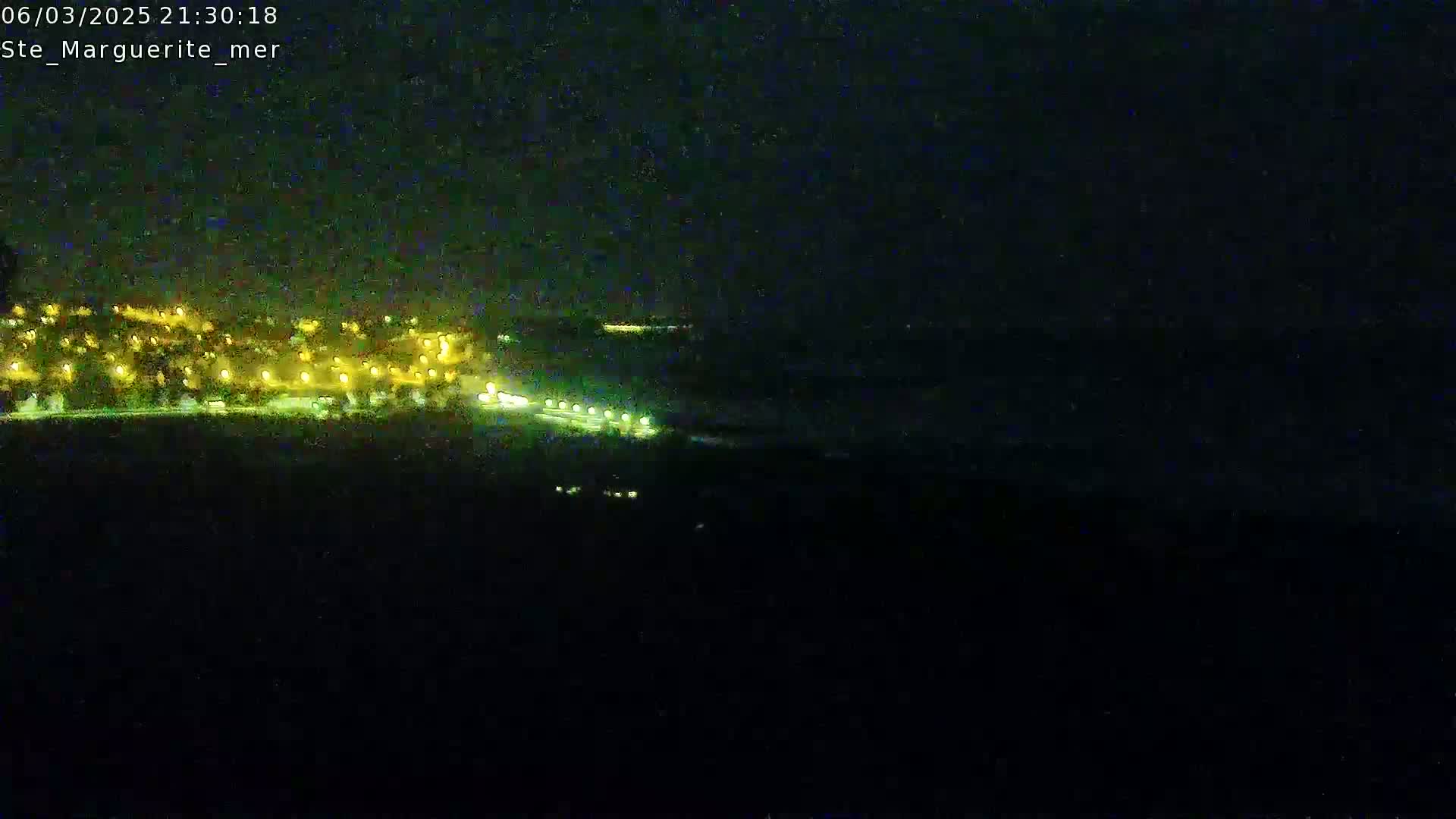 A nighttime long shot shows a dark coastline with a town's lights visible in the distance.