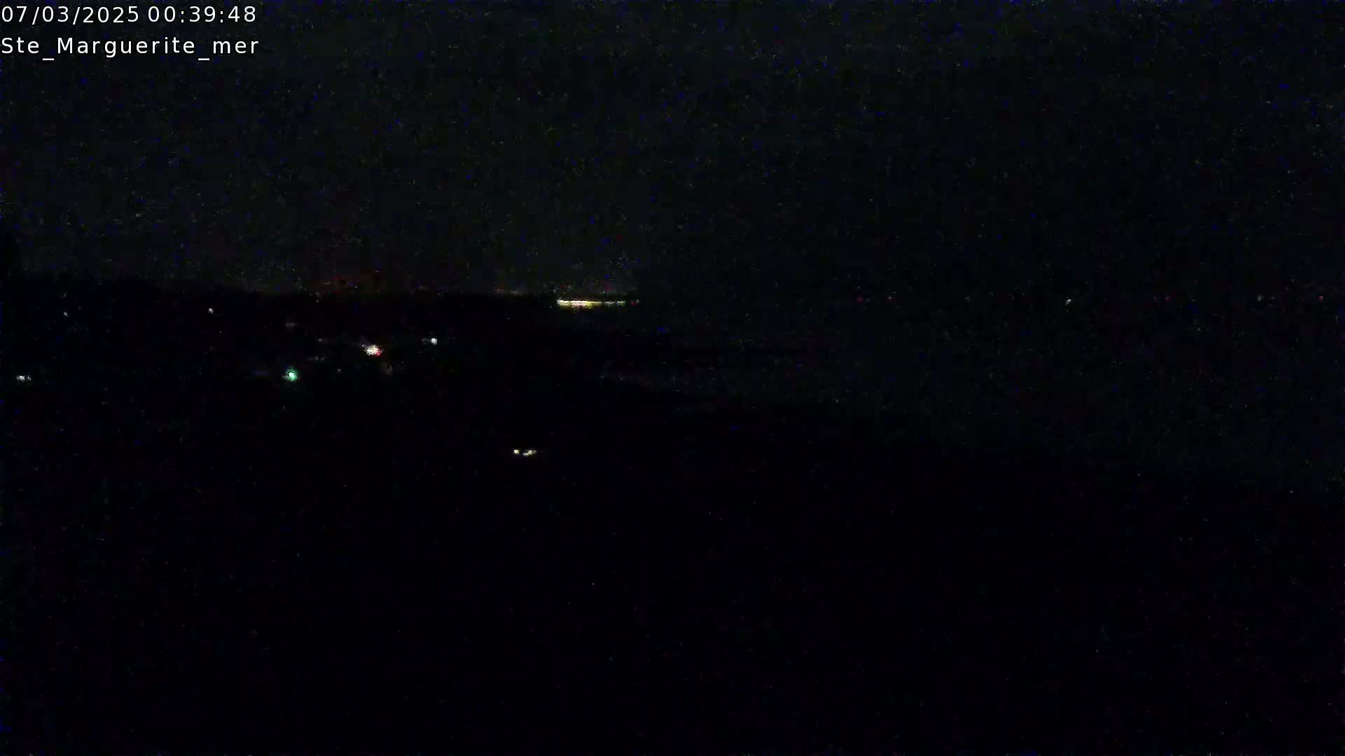 A nighttime, dark scene shows a distant line of lights on the horizon.