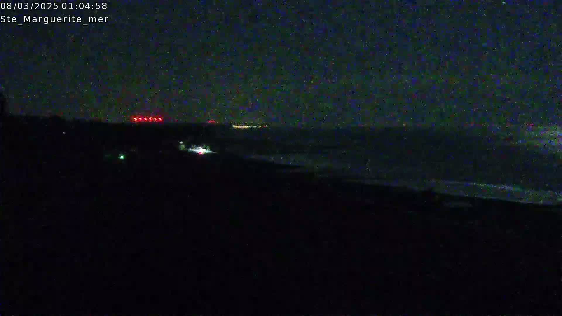 A dark nighttime scene shows a body of water with a shoreline, and faint lights are visible in the distance.