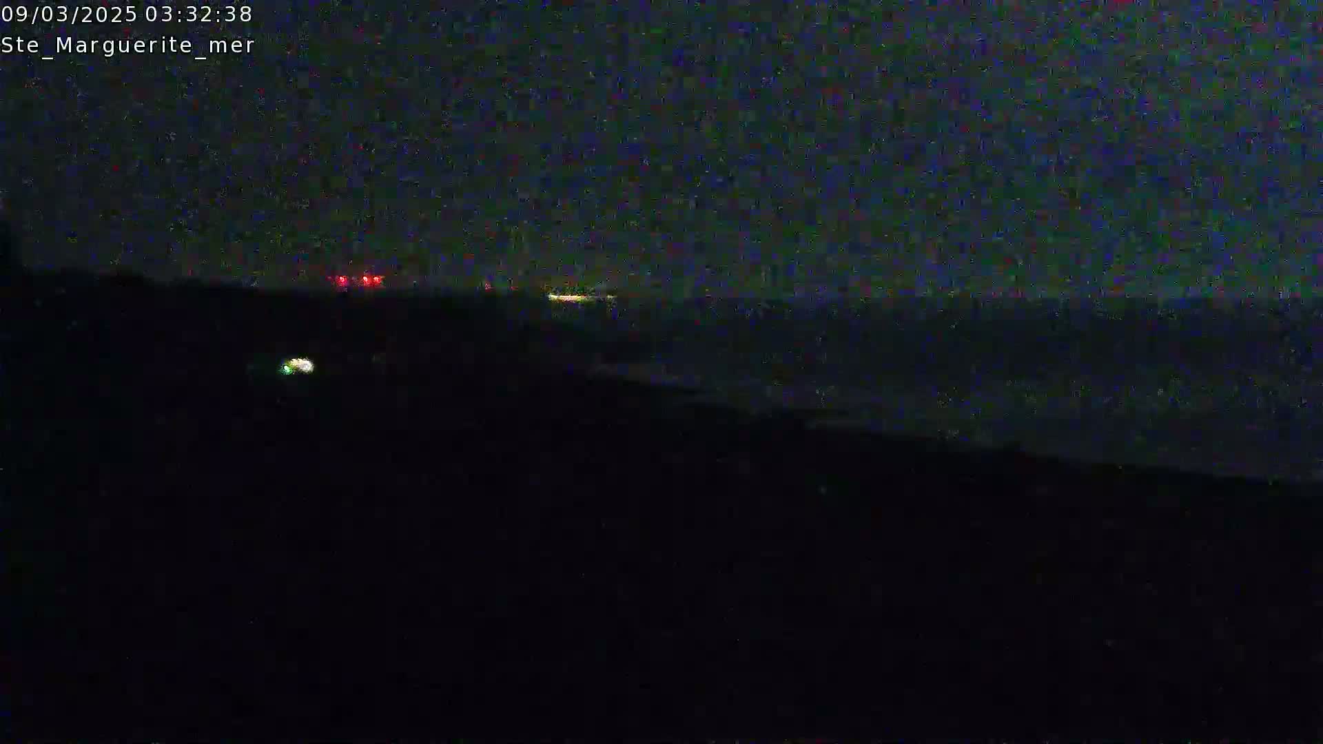 A dark, nighttime scene shows a body of water with faint lights on the horizon under a mostly clear sky.