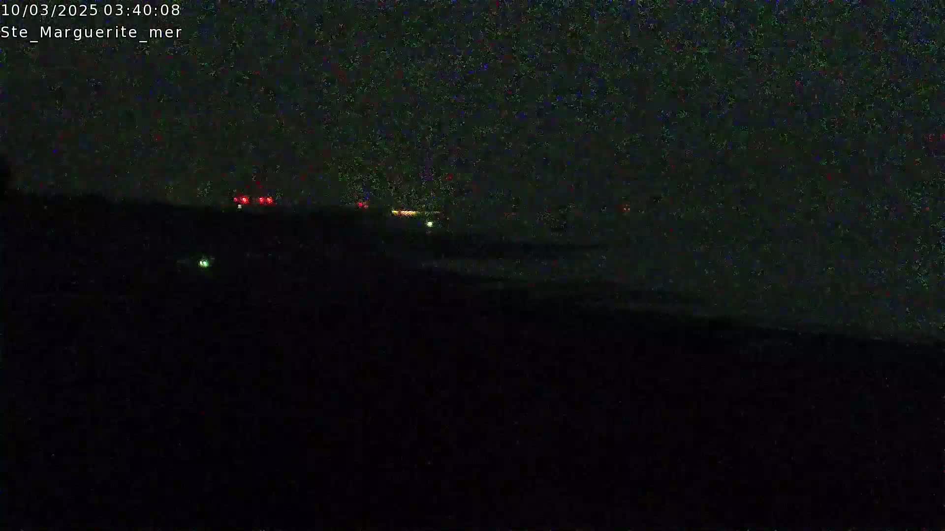 A dark, nighttime landscape is shown with a few faint lights visible in the distance.