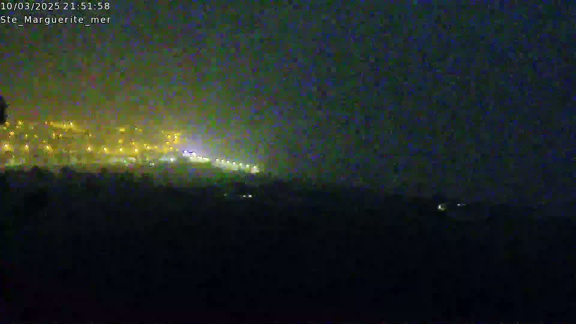 A hazy night scene shows a distant line of lights on a hill, possibly a road or buildings, under a dark sky.