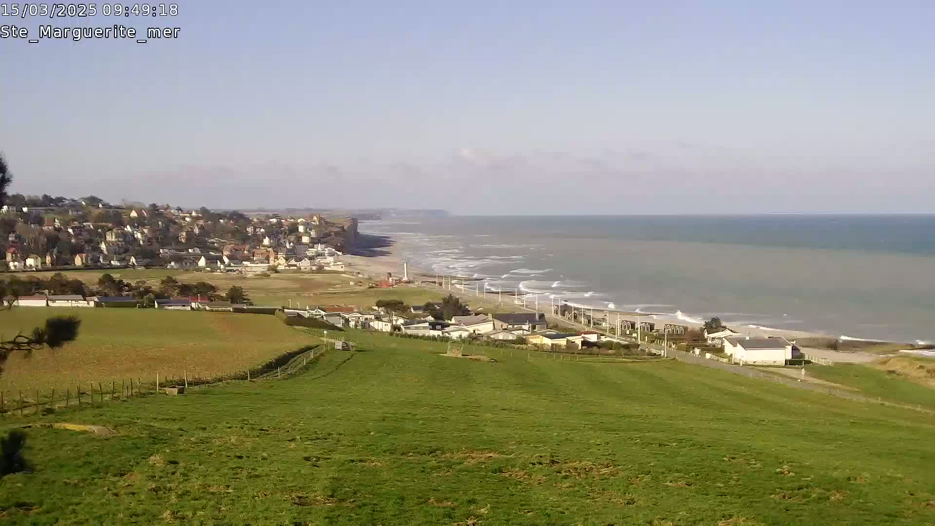 A coastal town nestled against a cliff overlooking a beach with gentle waves under a clear sky.