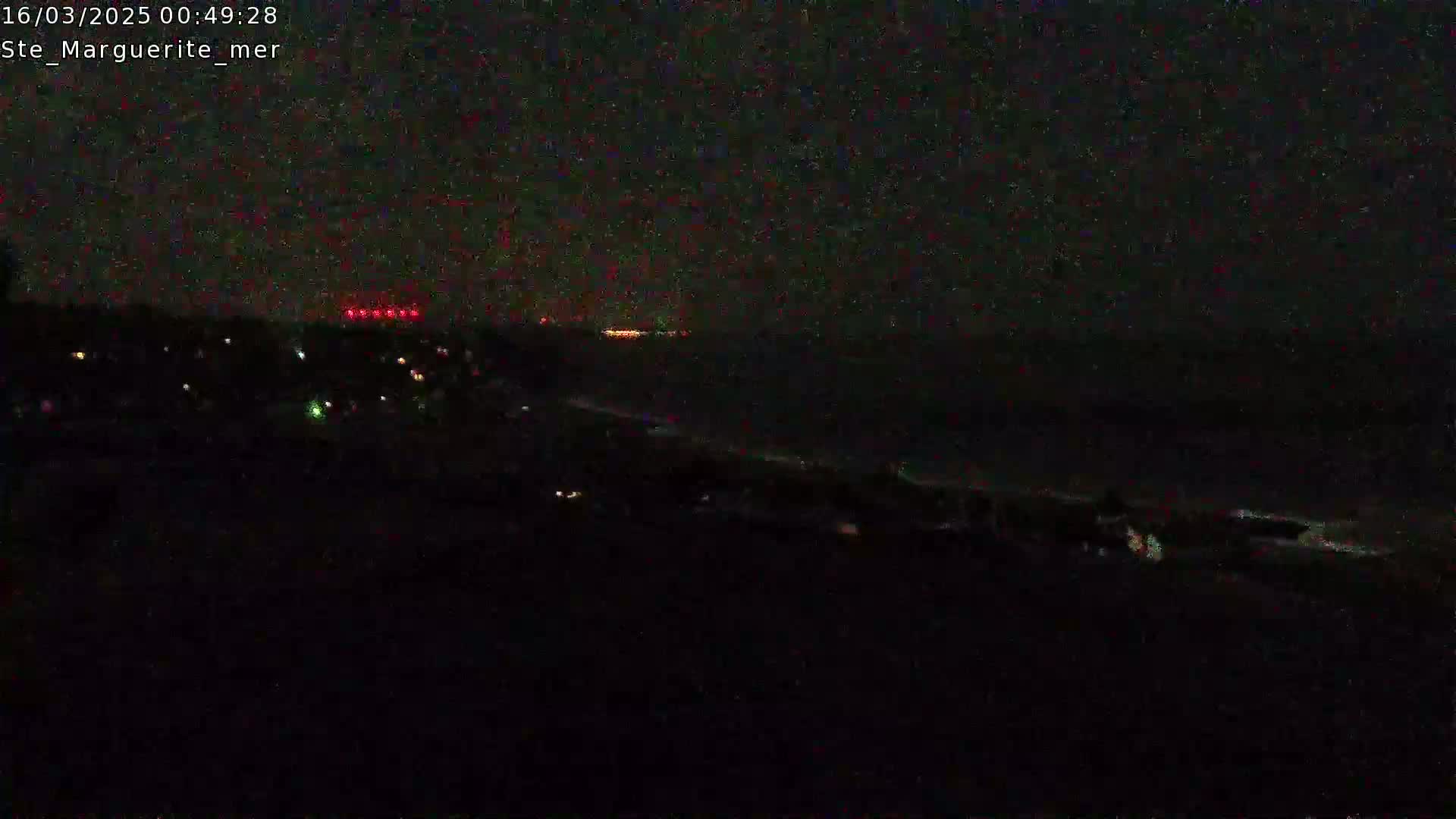 A dark nighttime scene shows a coastline with a few faint lights visible, and a dark body of water extending to a distant horizon where more lights are faintly visible.