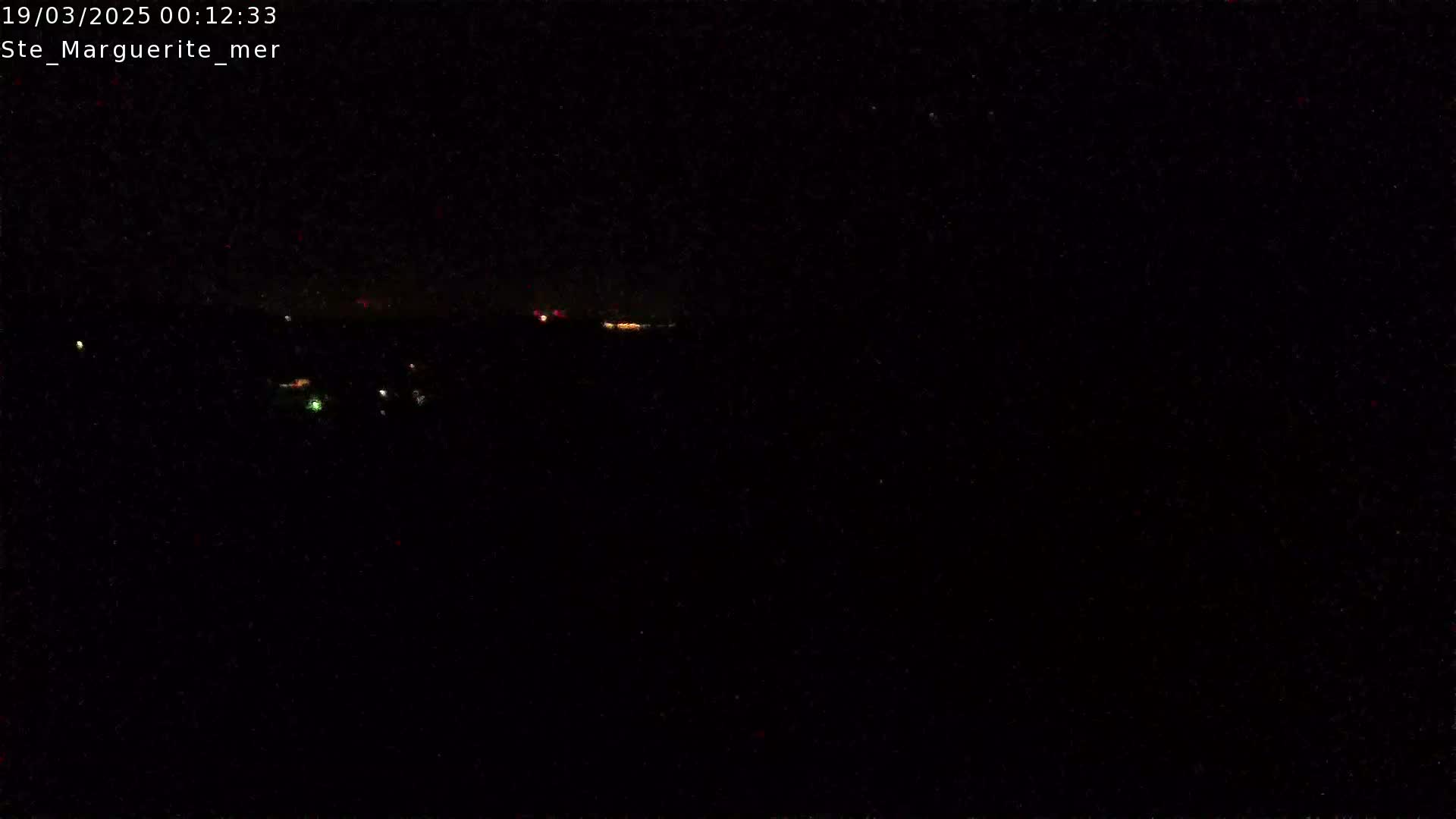 A nighttime, dark view shows a few distant, faint lights on the horizon under a clear, dark sky.