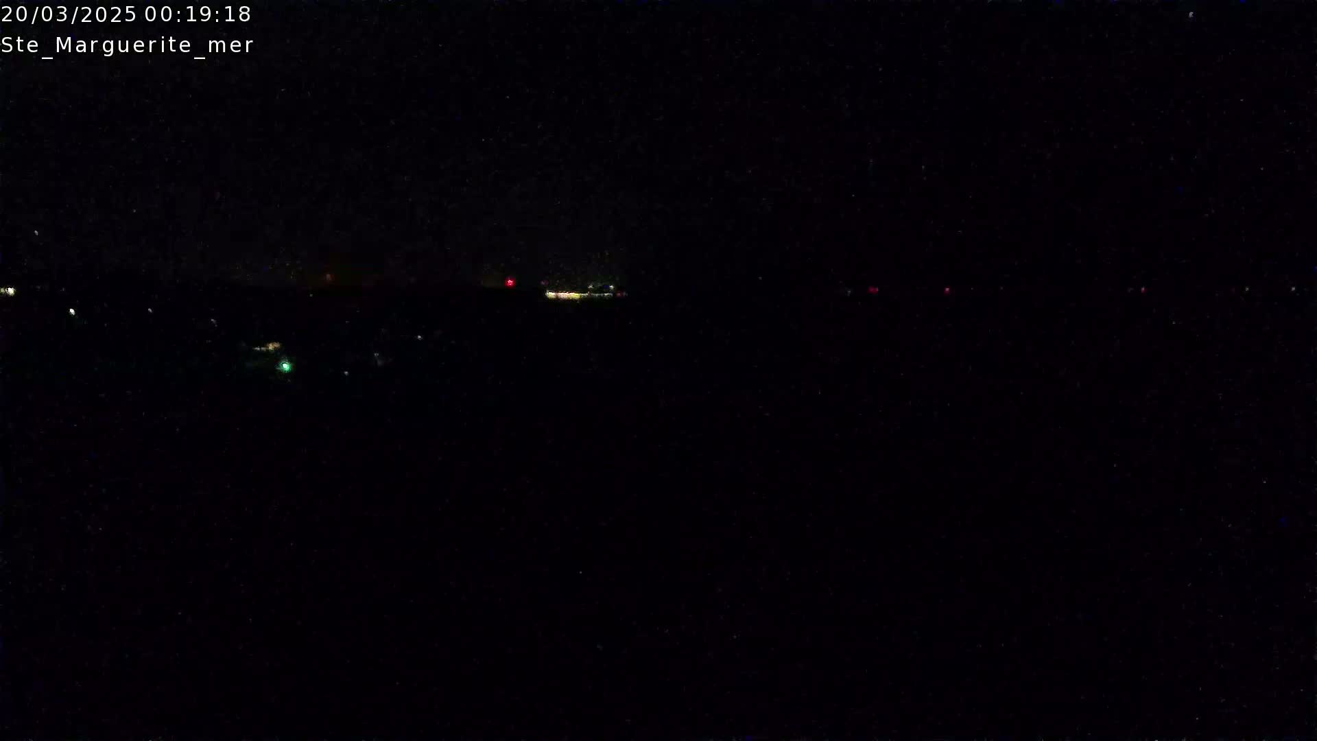 A nighttime long shot of a dark landscape with a few distant lights visible under a clear, dark sky.