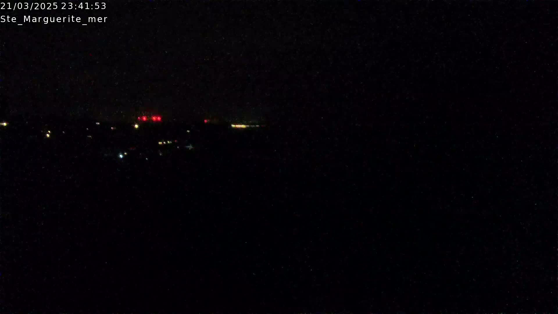 A nighttime long shot shows a dark landscape with a few faint lights in the distance under a clear, dark sky.