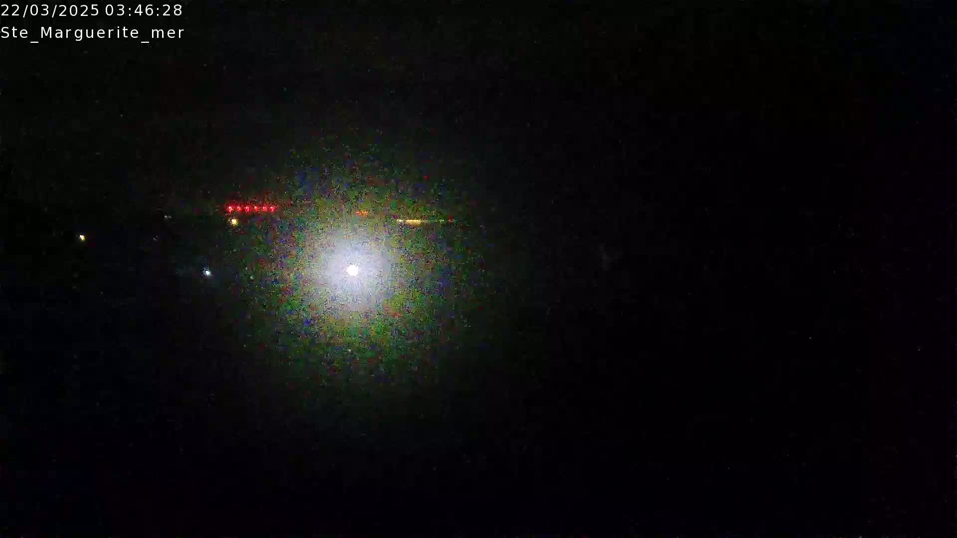 A bright light shines in the center of a dark, nighttime scene with a few faint lights in the distance.