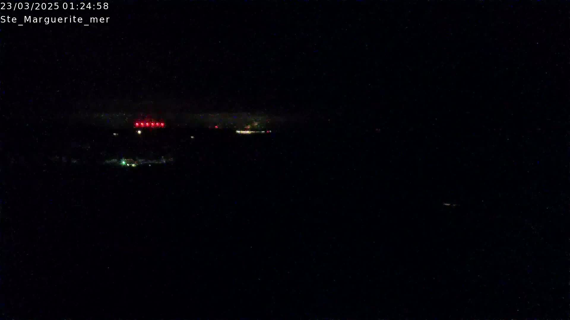 A nighttime, dark, outdoor scene shows a few faint lights in the distance.