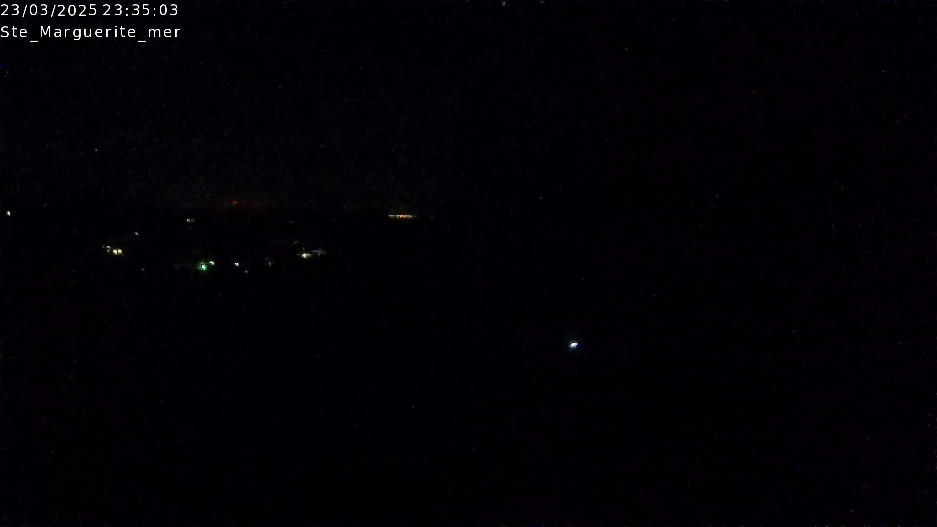 A dark, nighttime scene shows a few distant lights and a bright point of light in the middle distance under a clear, dark sky.